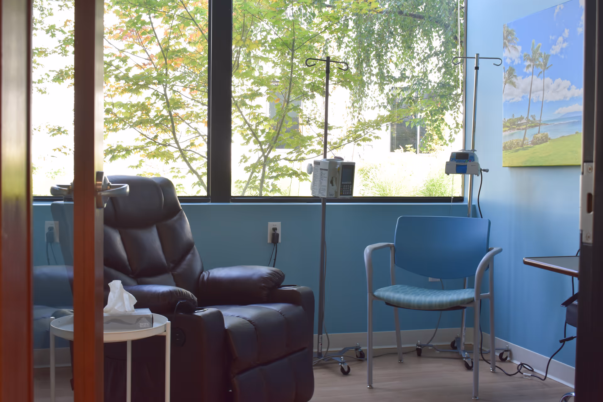 Infusion treatment room with a reclining chair, IV poles, blue walls, and large windows