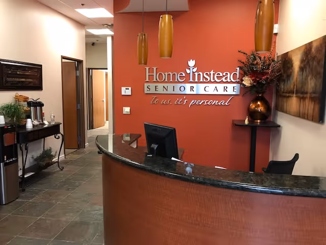 Curved reception desk in a warm lobby with a red wall and Home Instead signage.