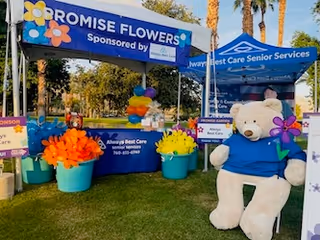 Outdoor event booth for Always Best Care Senior Services with a teddy bear and flower pots.