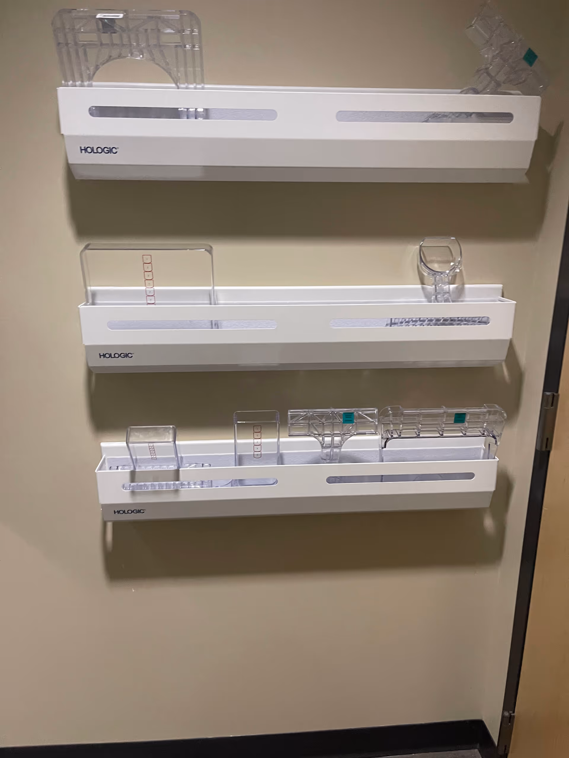 Wall-mounted medical supply racks labeled Hologic with clear plastic organizers.