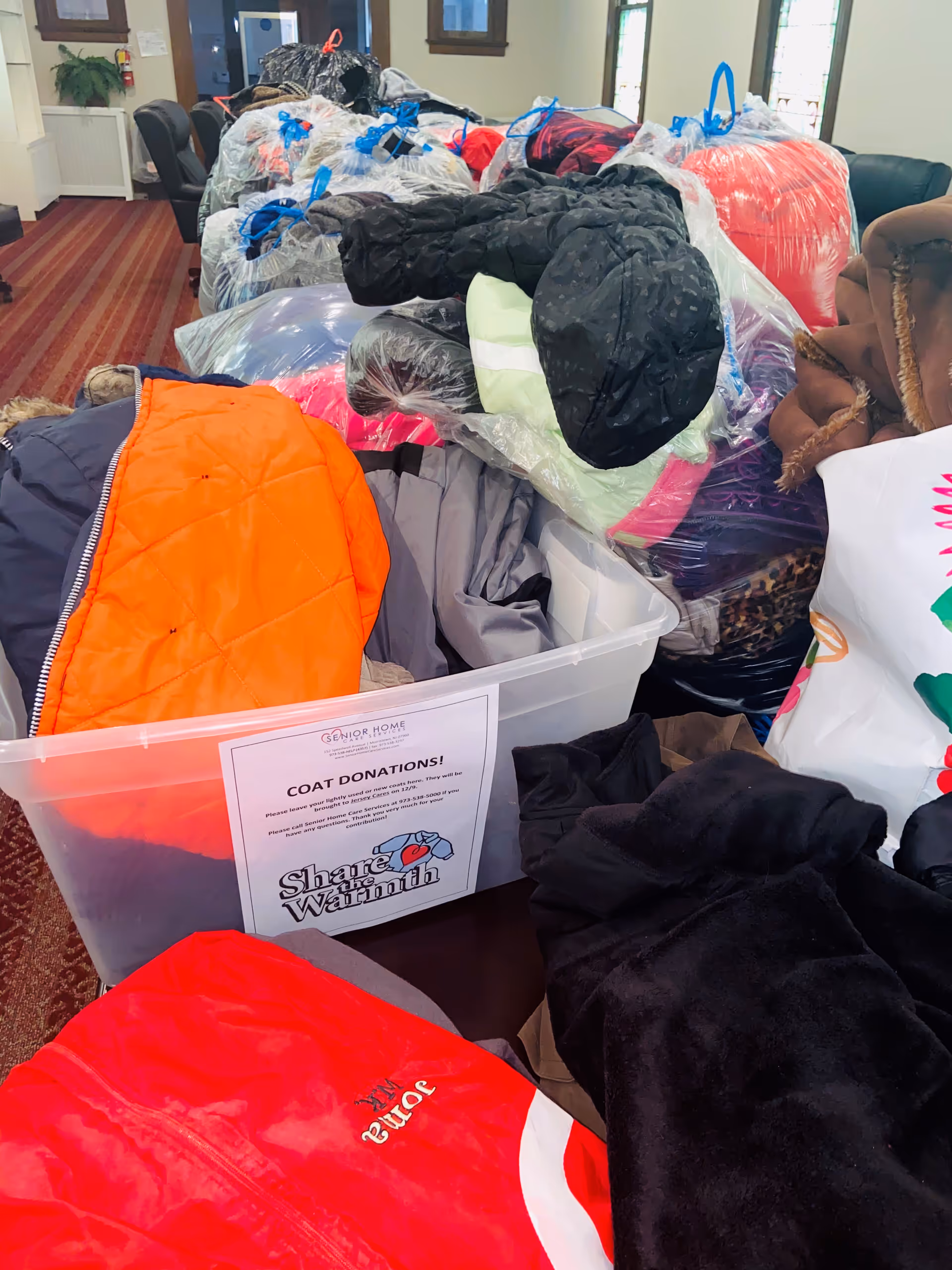 Pile of donated coats and bags filling a room inside a senior living facility.