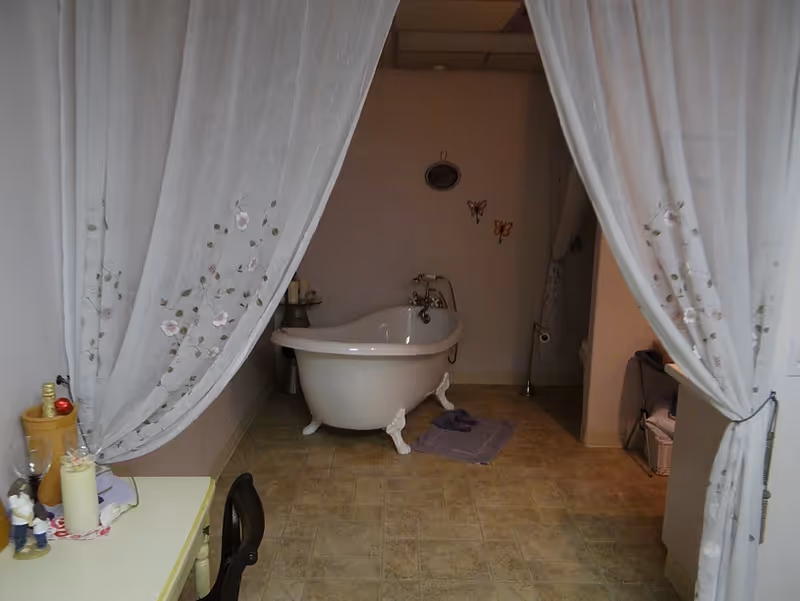 A freestanding clawfoot bathtub enclosed by sheer curtains in a tiled bathroom.