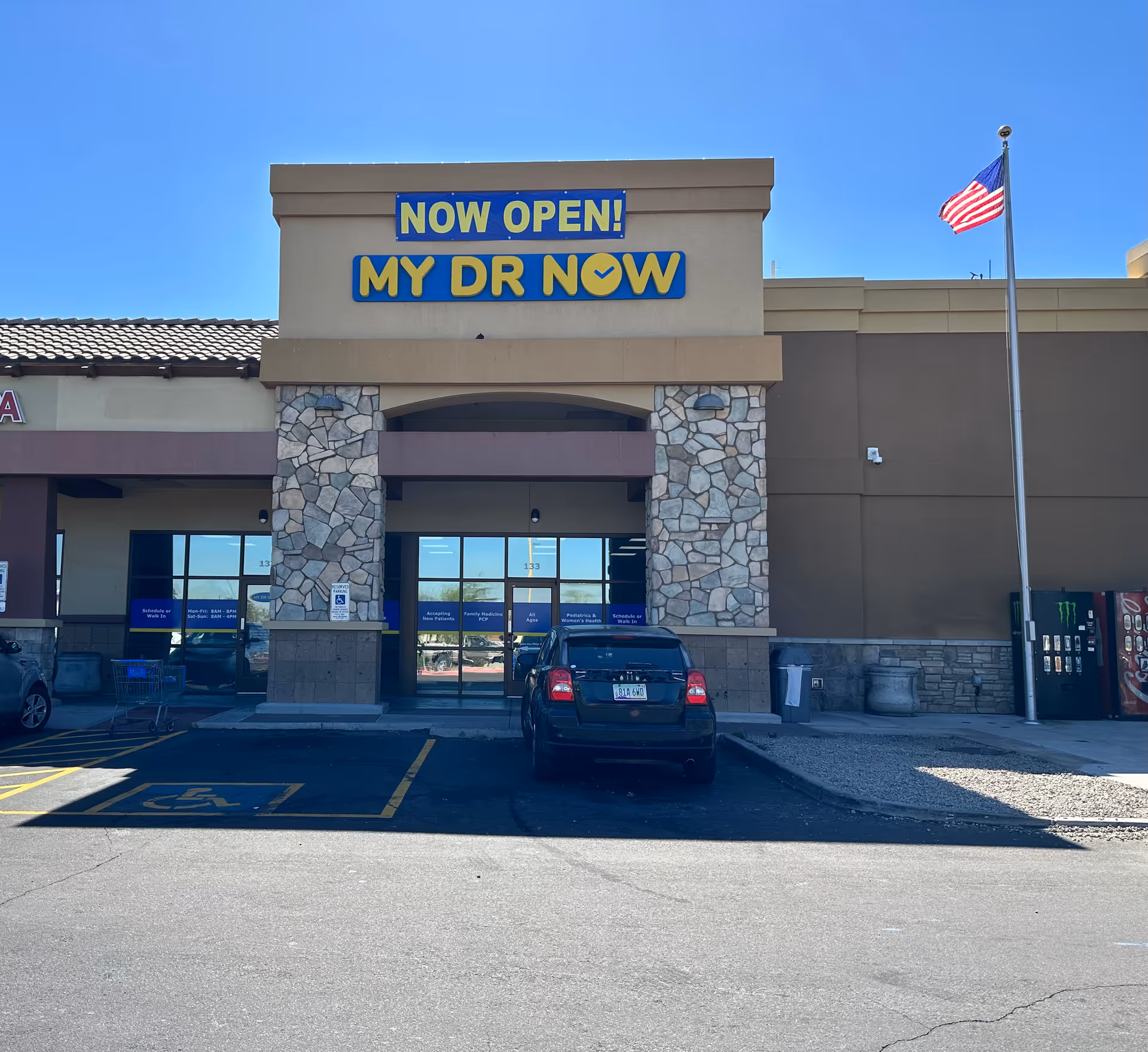 Front of a building with NOW OPEN! MY DR NOW sign and parking lot.