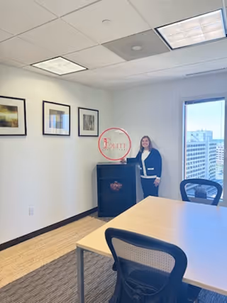 Staff member stands near a cabinet in a bright conference room with framed pictures.