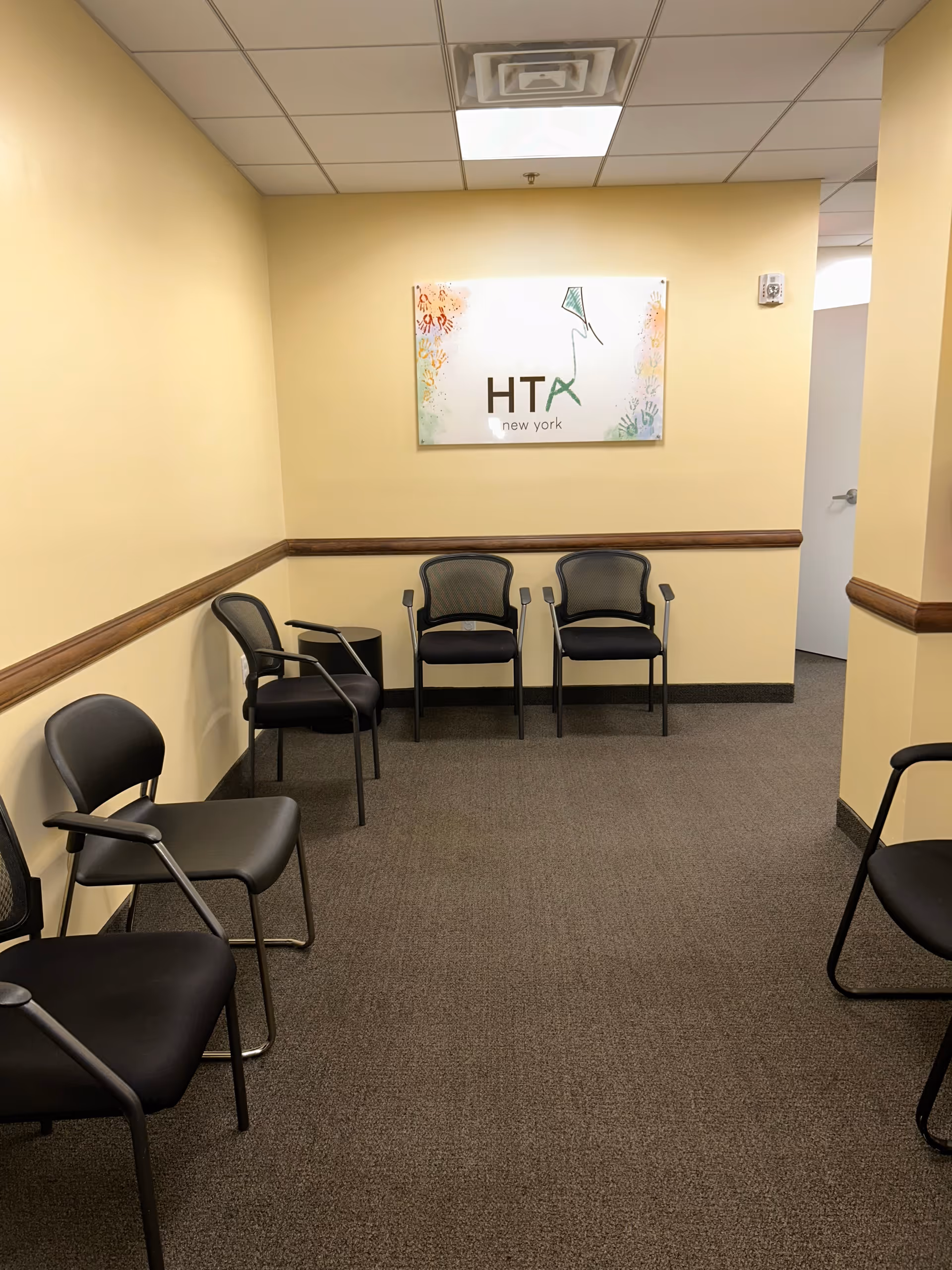A small waiting area with black chairs along beige walls and a colorful sign.