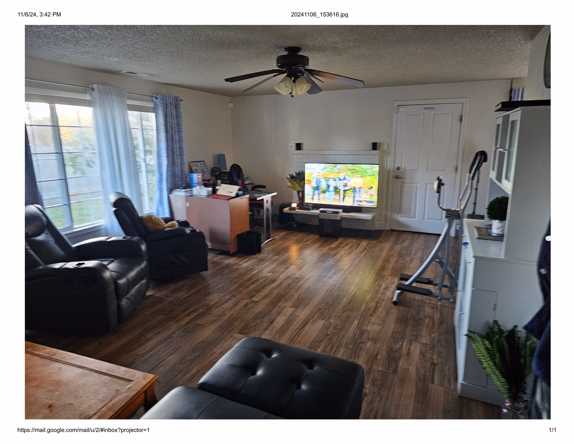 Spacious living room with recliners, a TV, exercise equipment, desk, and large windows.