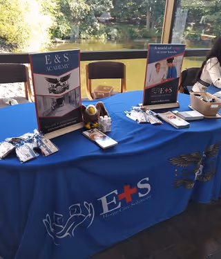 Promotional table draped in blue with E&S Academy brochures near a sunlit window.