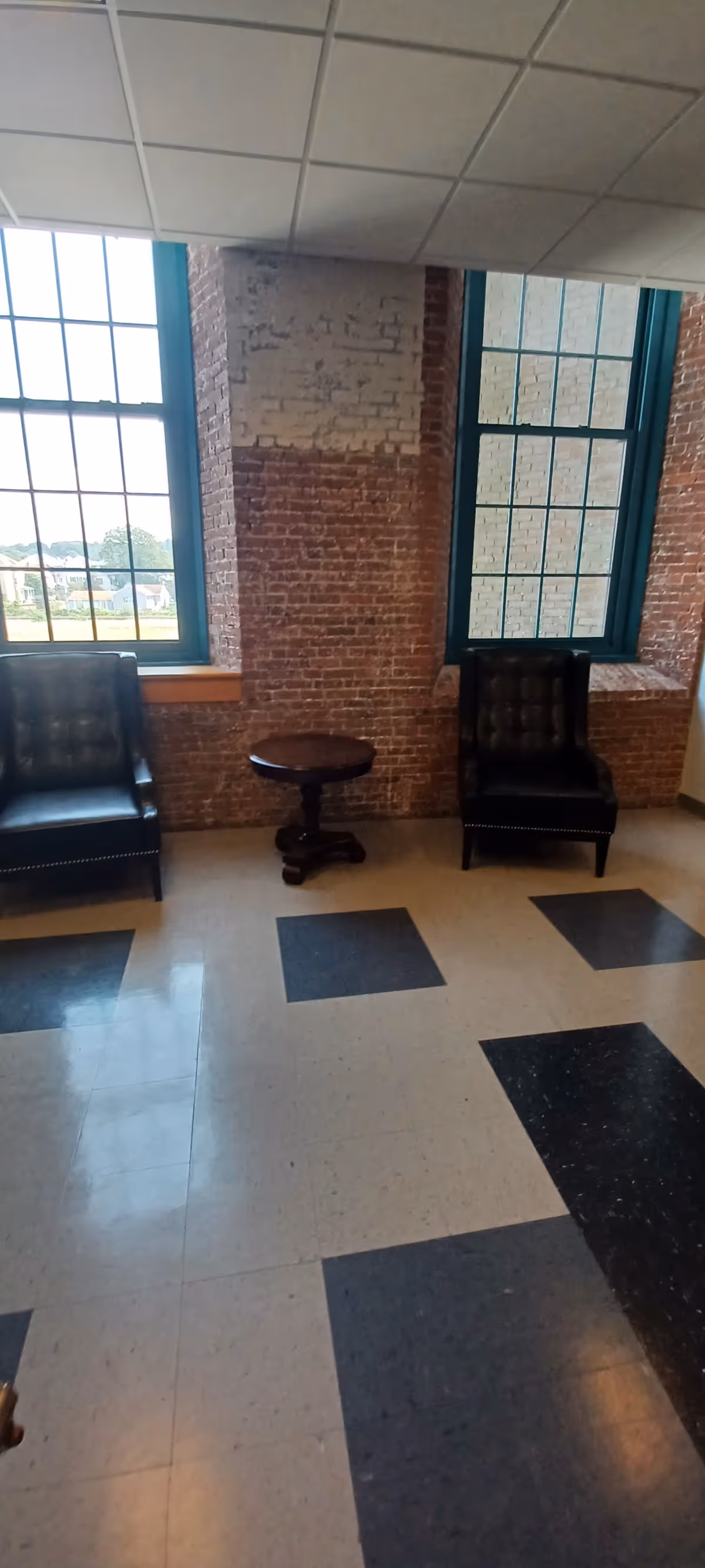 Two dark chairs flank a round table by brick-walled windows in a bright interior.