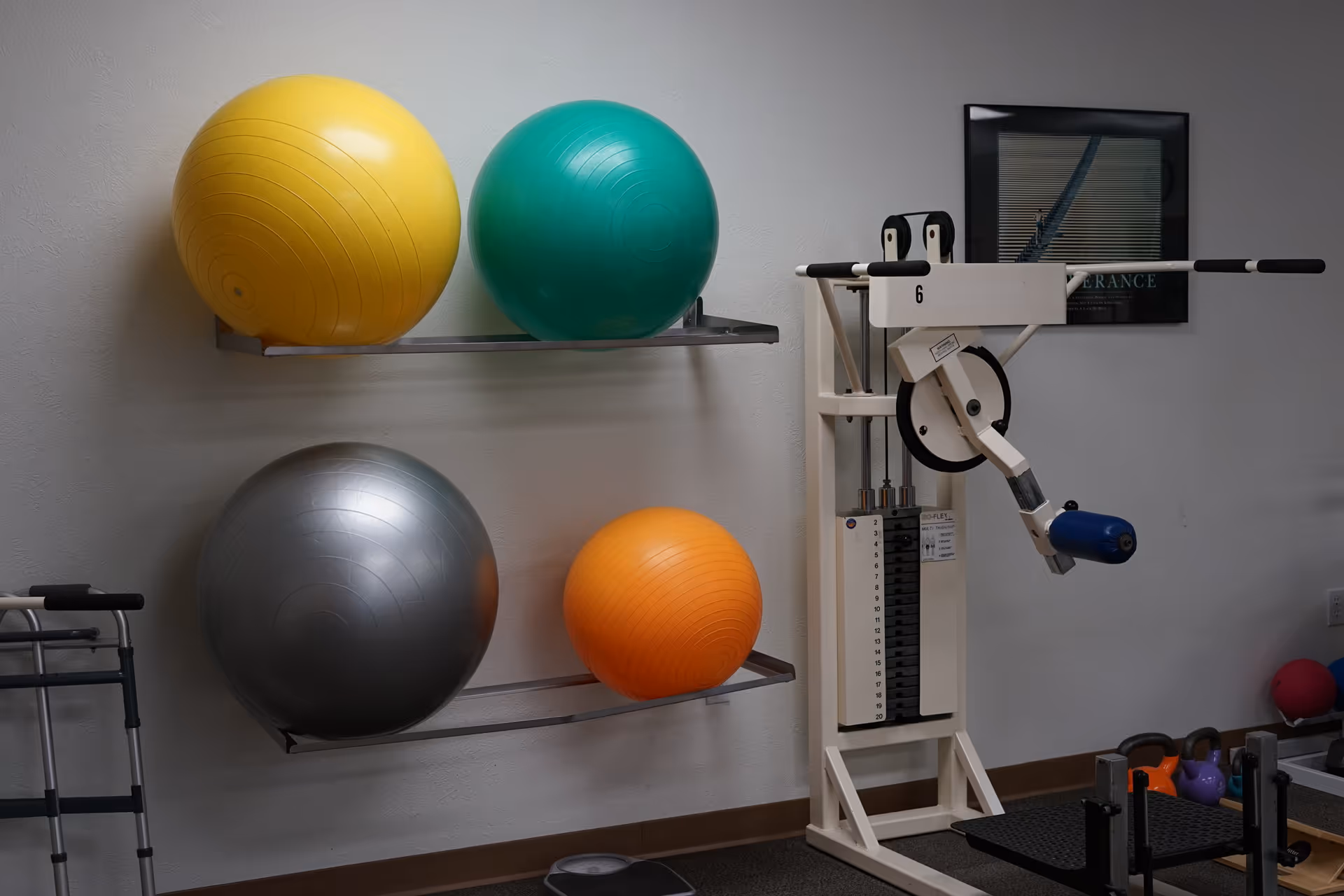 Physical therapy room with colorful exercise balls on wall shelves and a weight machine.