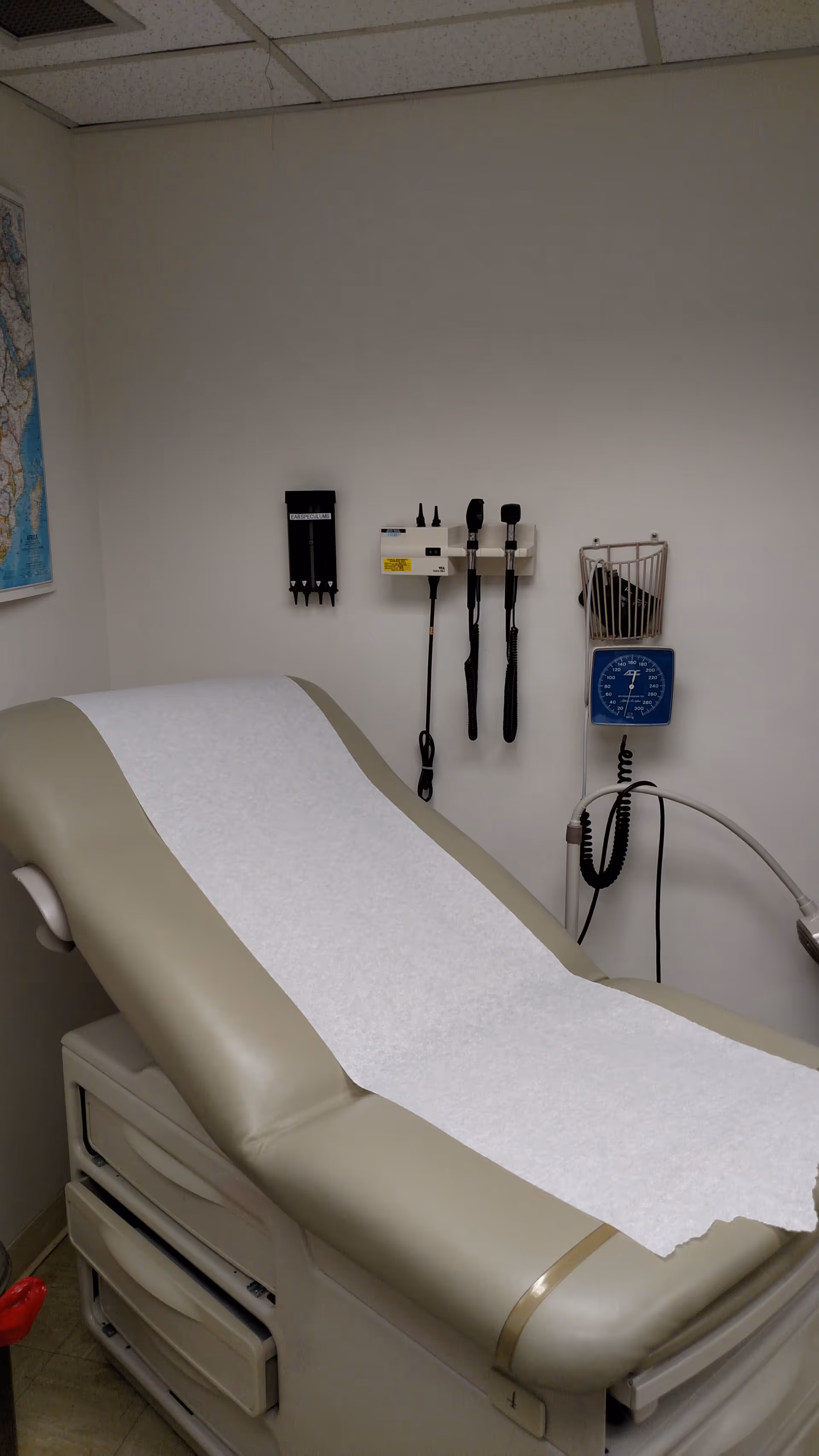 Clinical examination bed with paper sheet and mounted medical instruments on the wall.