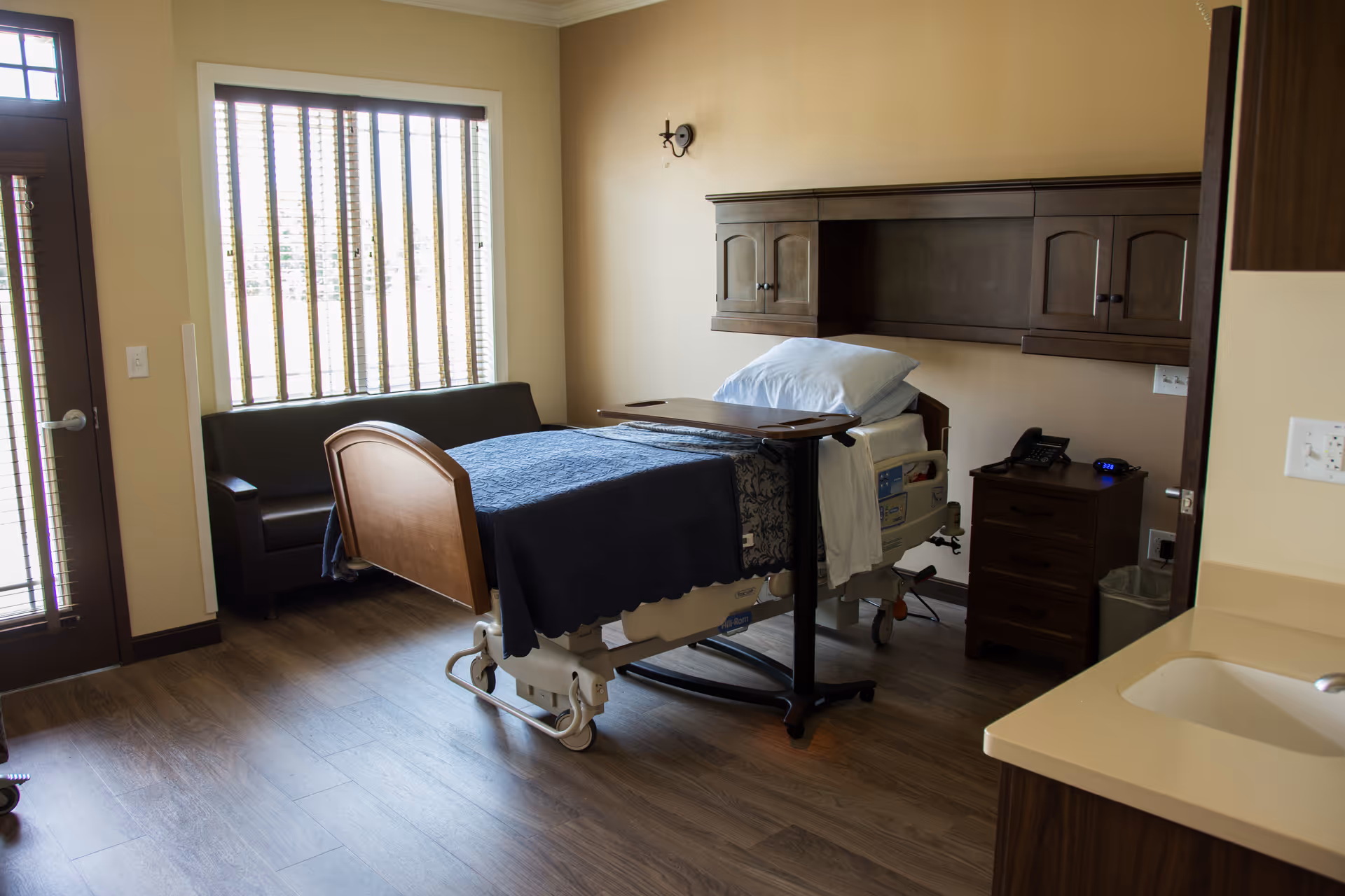 A hospital-style patient room with an adjustable bed, sofa, and cabinets.