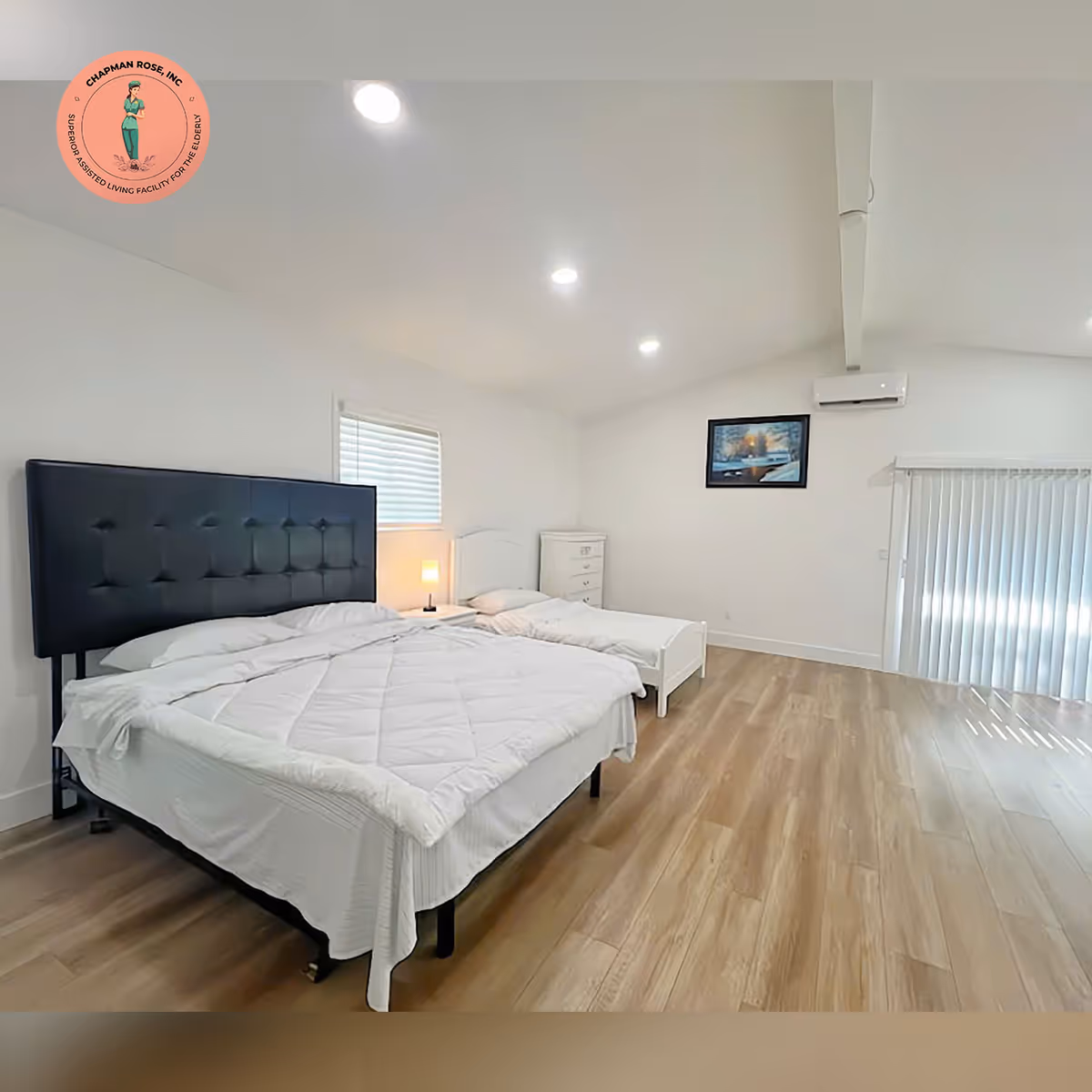 This bright bedroom features two white beds, a dresser, and wall art.