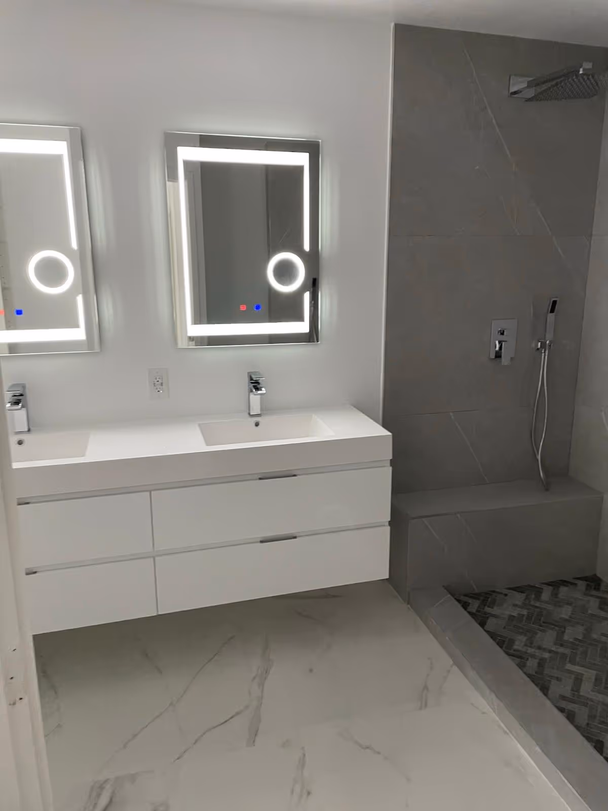 Modern white bathroom with double sinks, backlit mirrors, and a glass-enclosed shower.