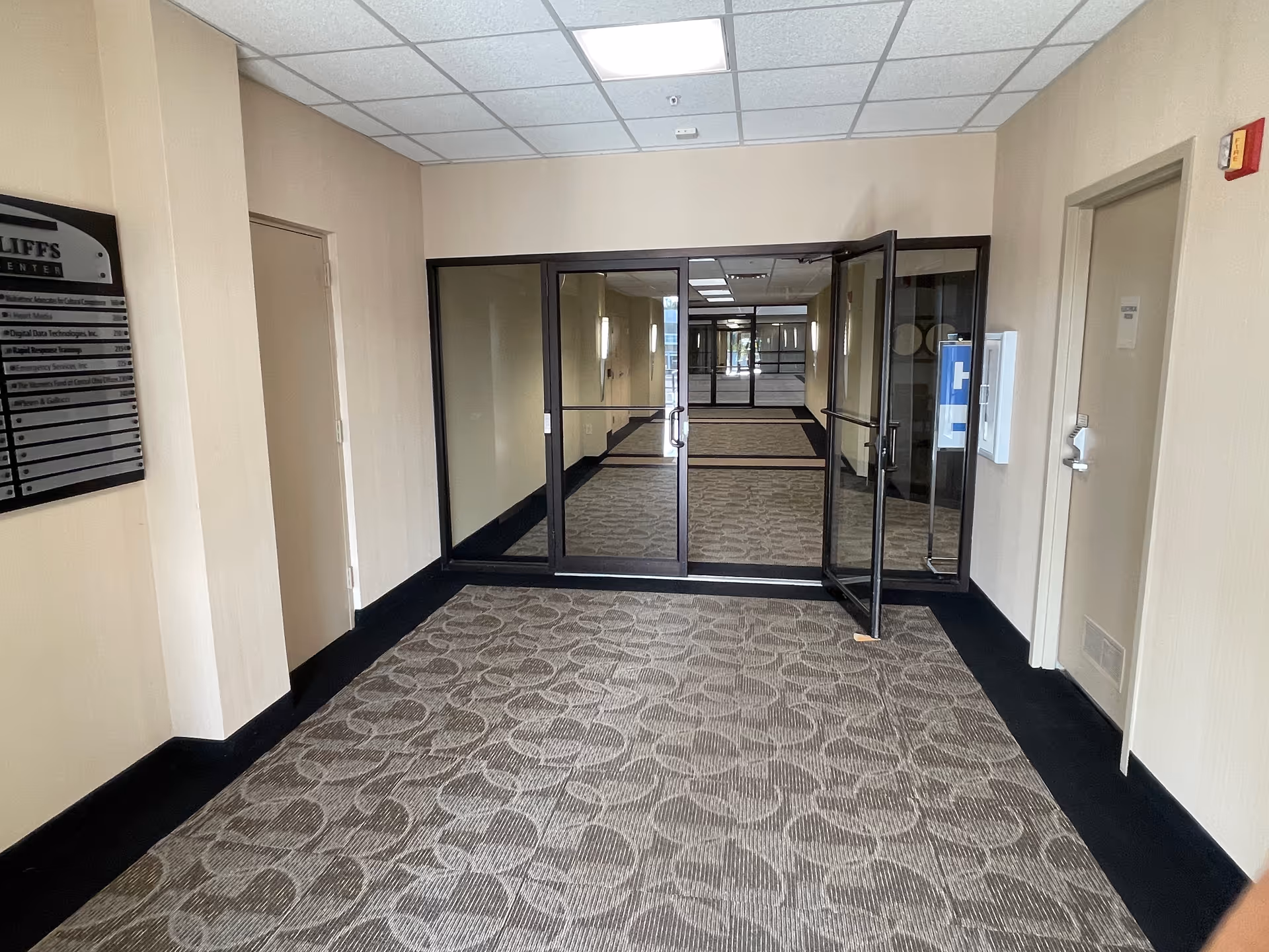 Hallway with glass doors, beige walls, and patterned carpet in a senior living facility.