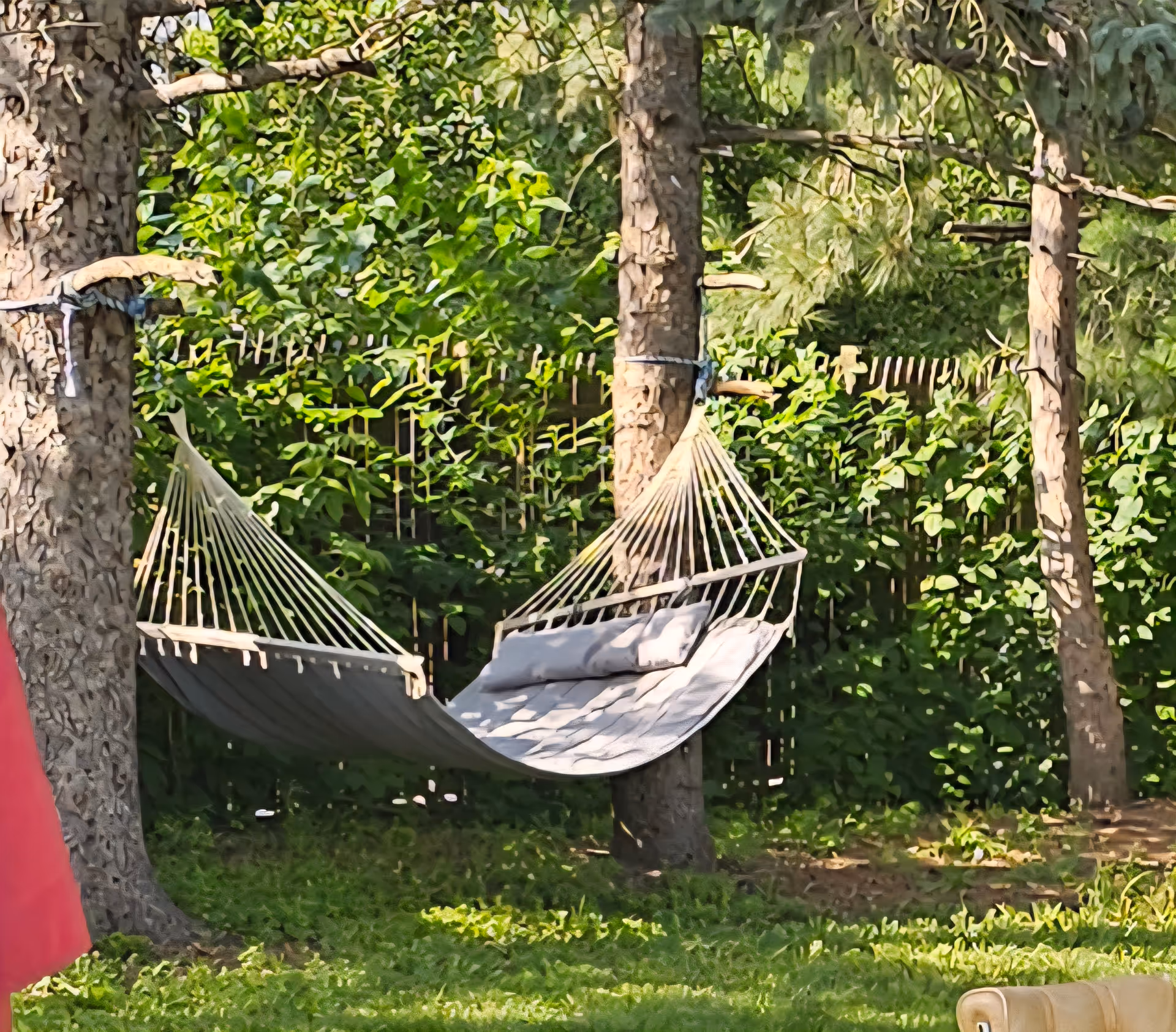 Two beige hammocks strung between trees in a grassy, shaded outdoor area.