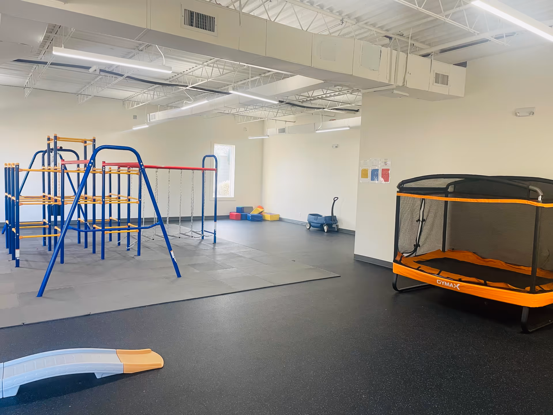 Indoor therapy space with blue climbing frame, trampoline, and padded play area.
