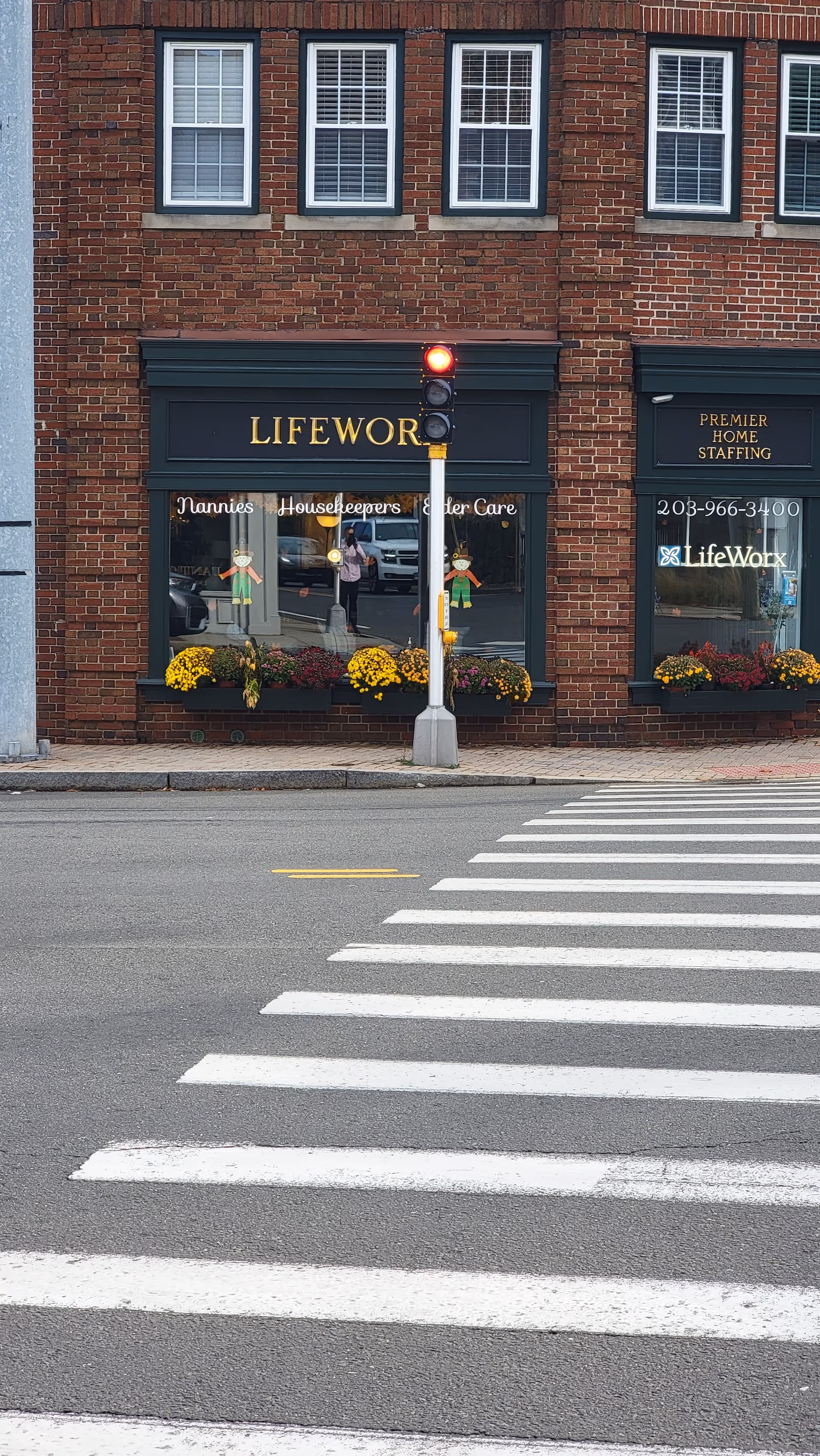 Brick storefront showing LifeWorx Home Care signage, traffic light, and flower planters.