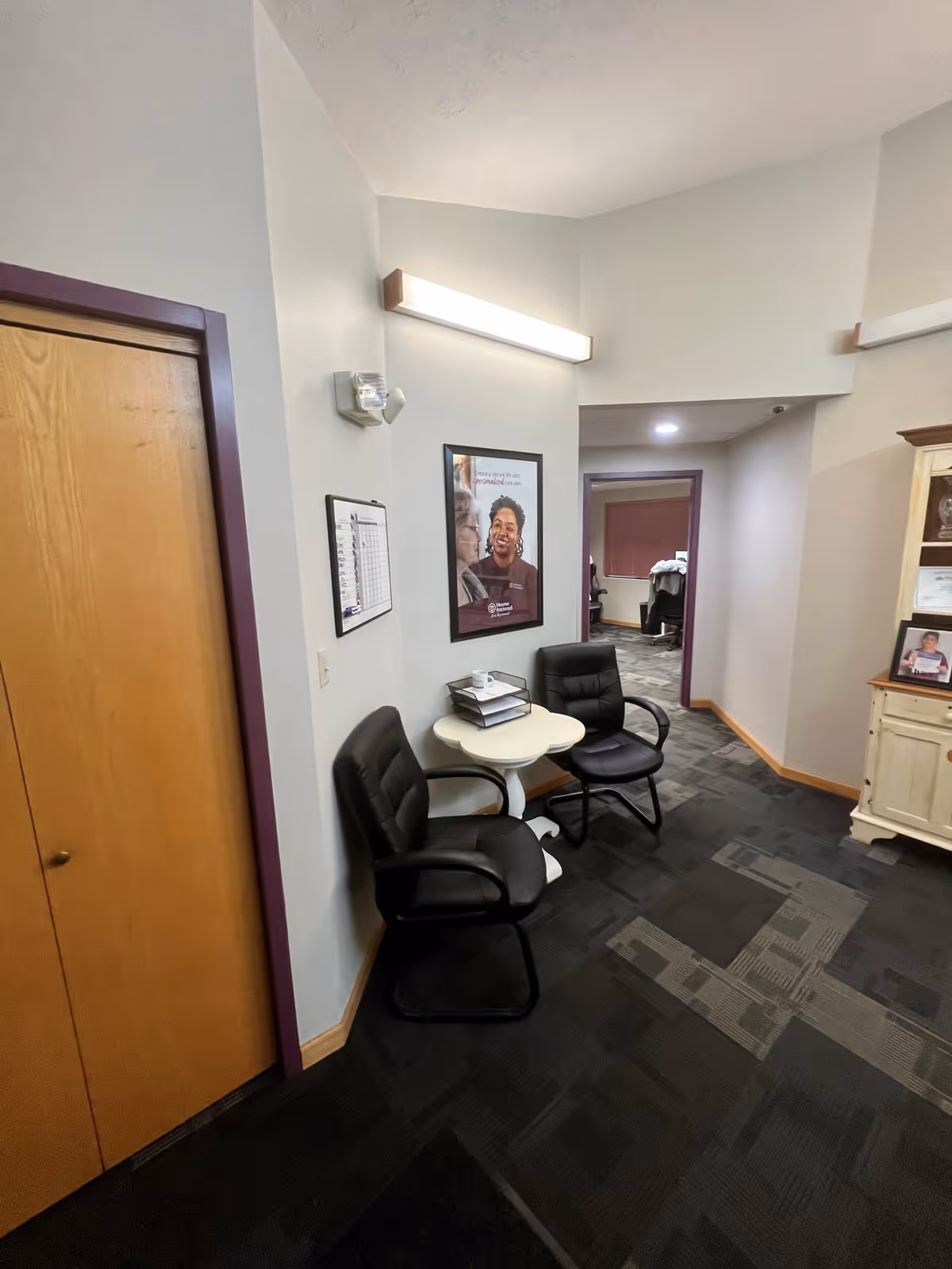 Interior hallway at a Home Instead facility with two black armchairs and a round table.