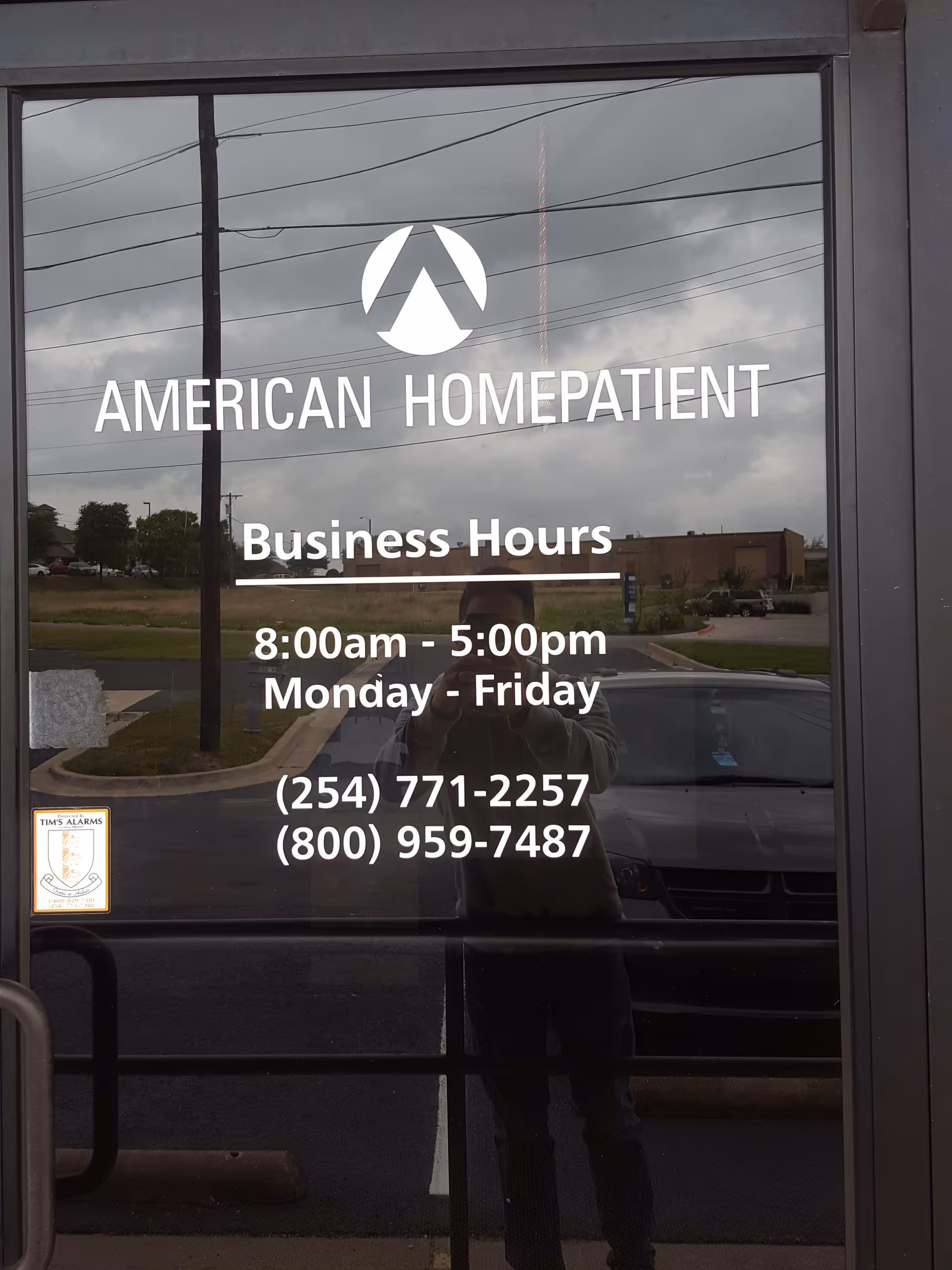 Glass door shows American HomePatient signage and business hours with photographer's reflection.