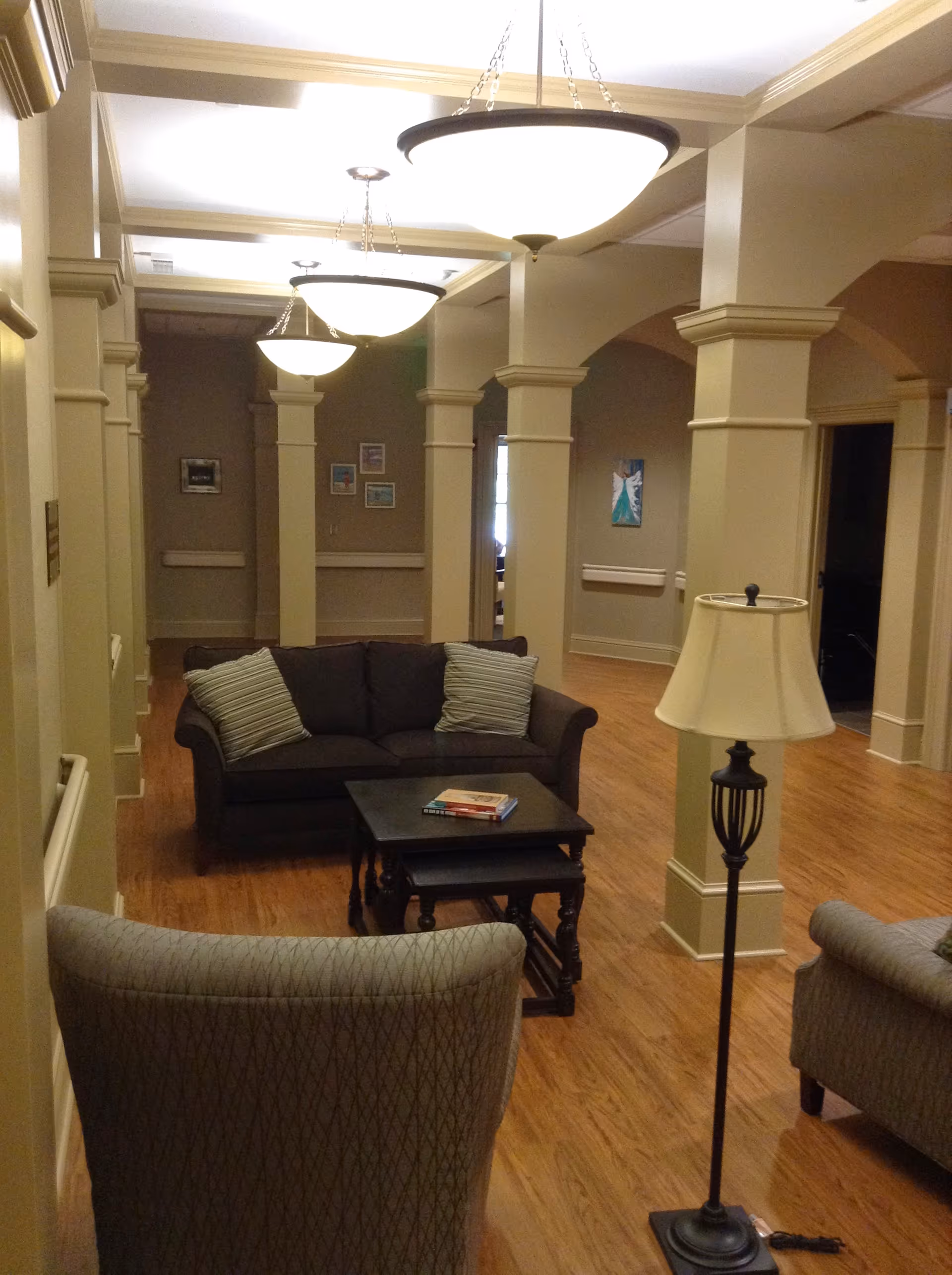 Interior lounge with couches, coffee table, lamps, and columns in a senior living facility.