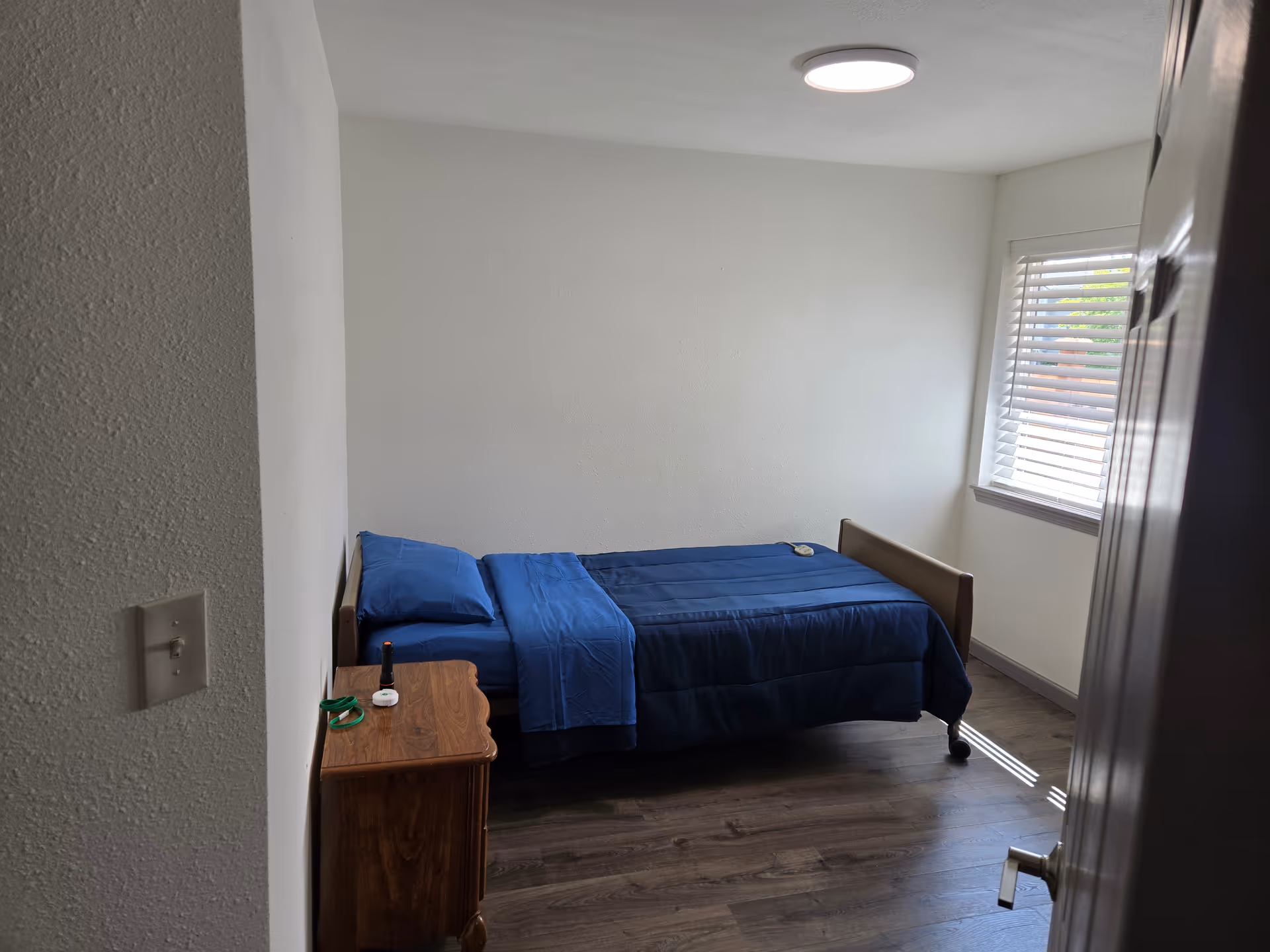 A small bedroom with a single bed, blue bedding, and a window with blinds.