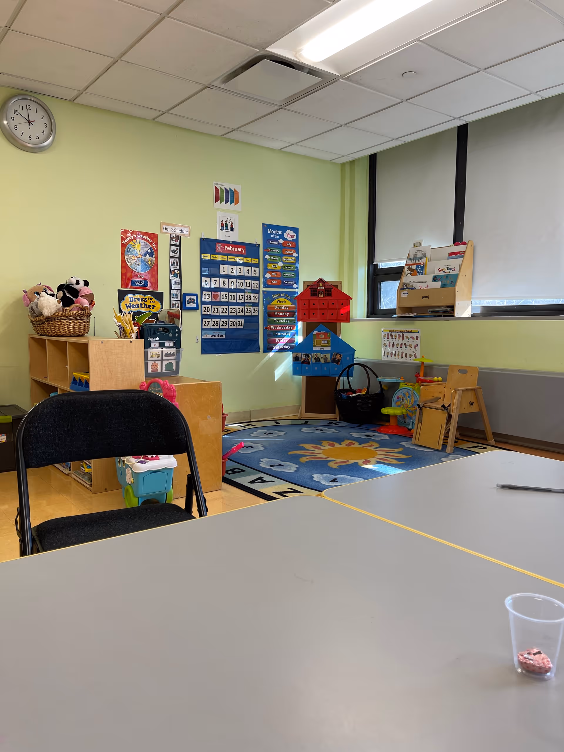 Bright pediatric playroom with toys, calendar charts, and a small table in foreground.