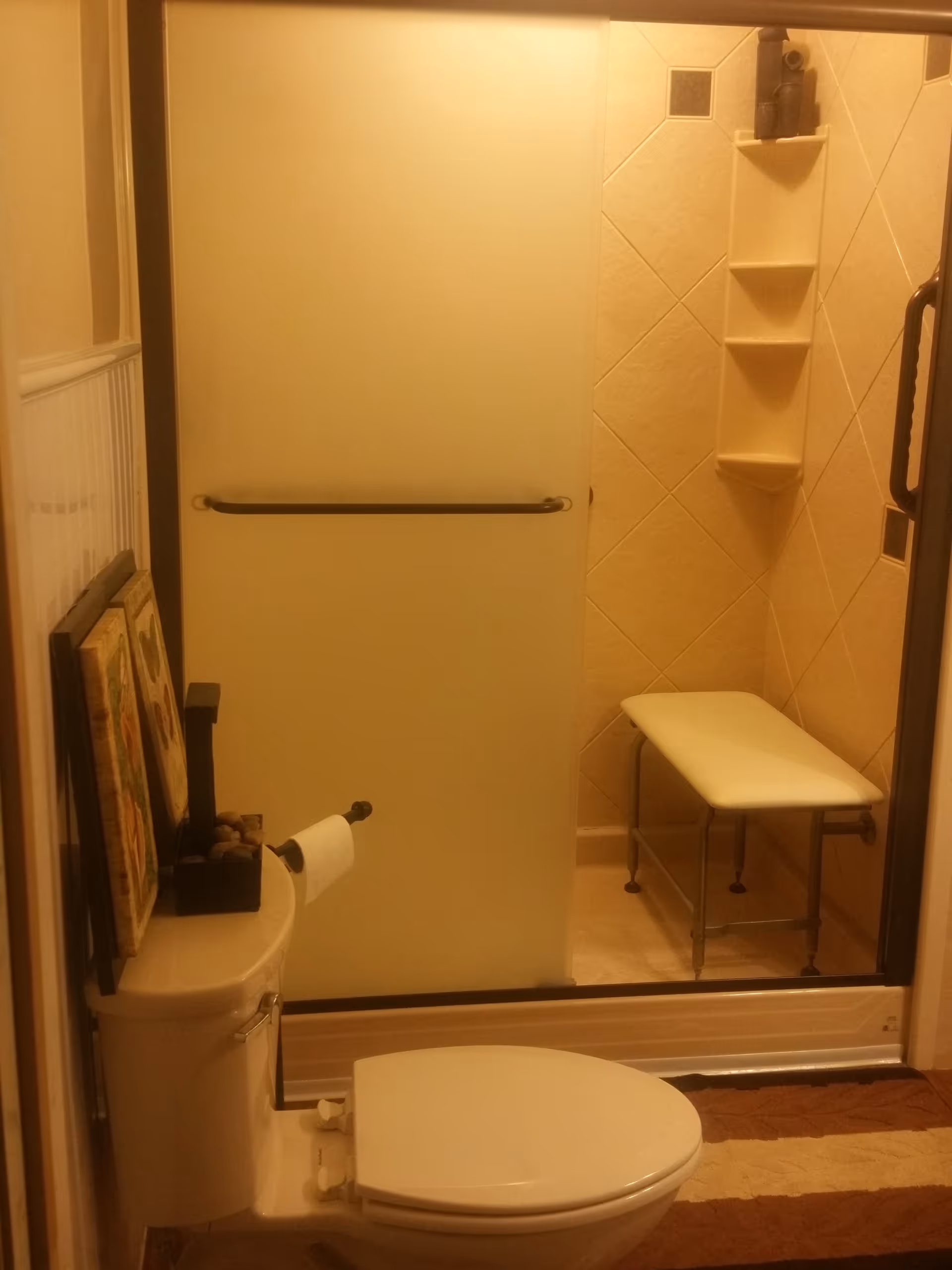 A compact bathroom with a sliding shower door, toilet, and a shower bench.