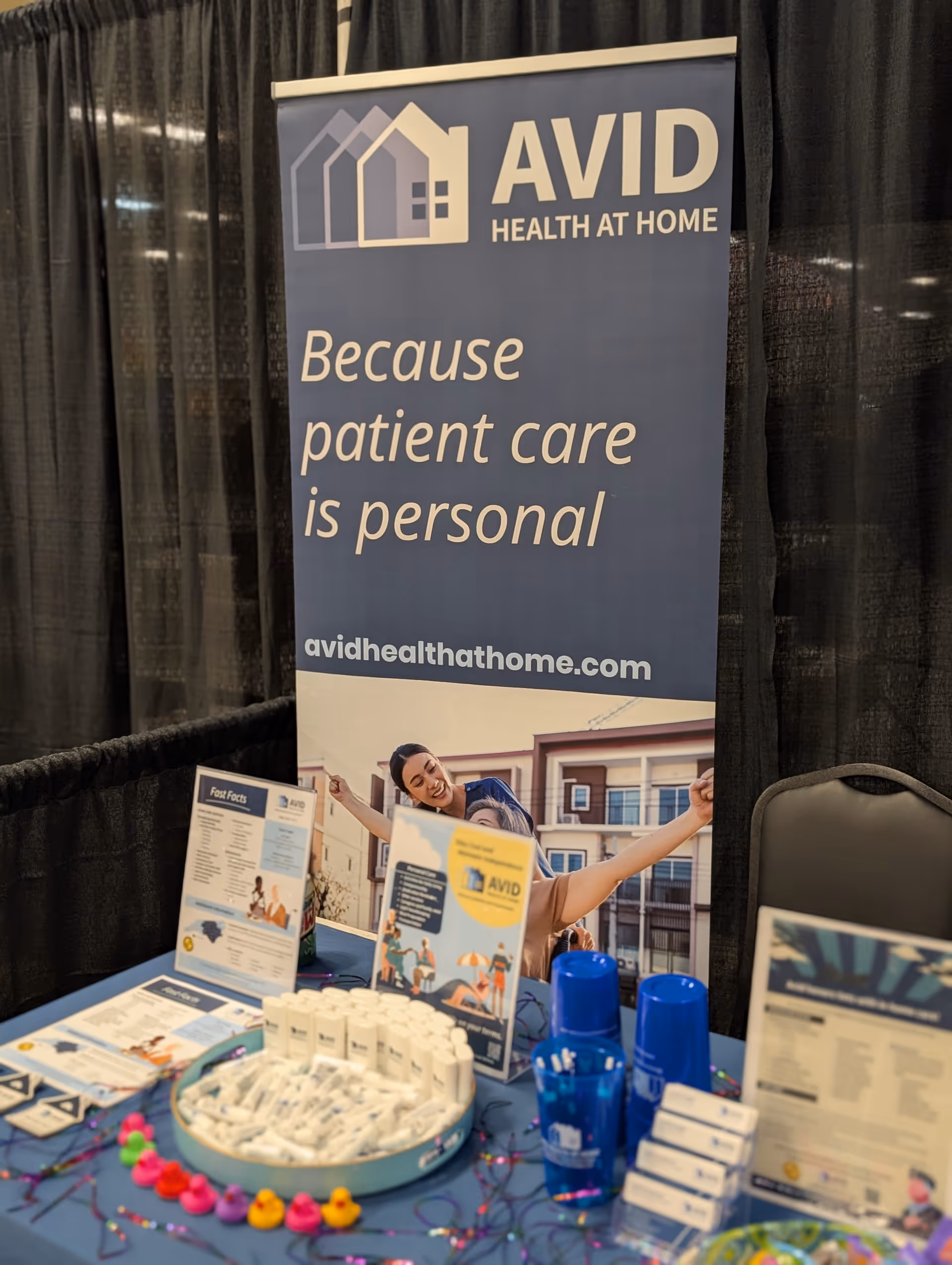 An Avid Health at Home booth with a banner and table full of informational materials.