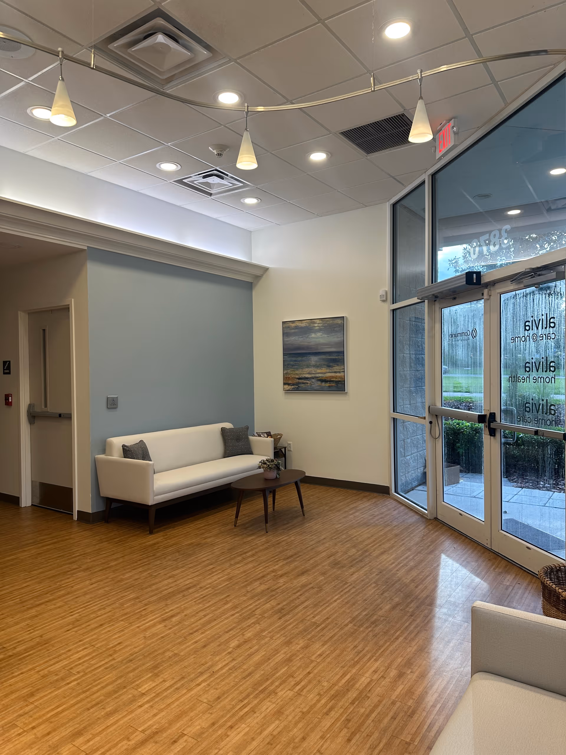 Modern interior lobby area with white sofa, coffee table, painting, and glass front entrance.