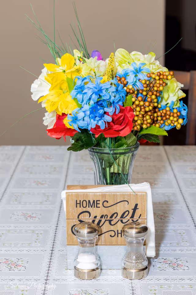 Colorful flower bouquet in a glass vase on a table with a Home Sweet Home sign.