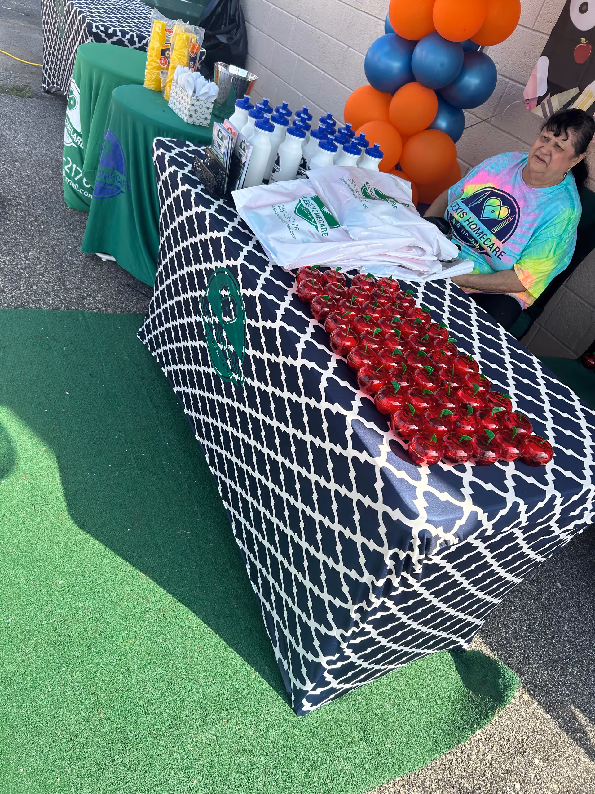 Outdoor event table with tomatoes, water bottles, swag bags; a woman nearby.
