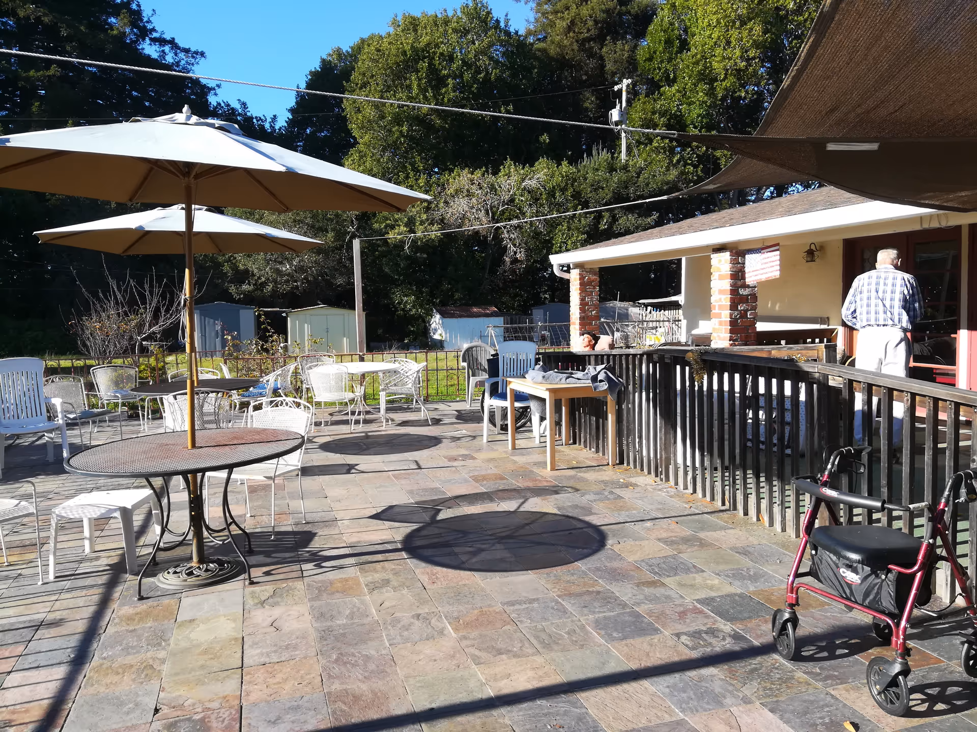 Sunny outdoor patio with tables, umbrellas, and a resident near a covered building.