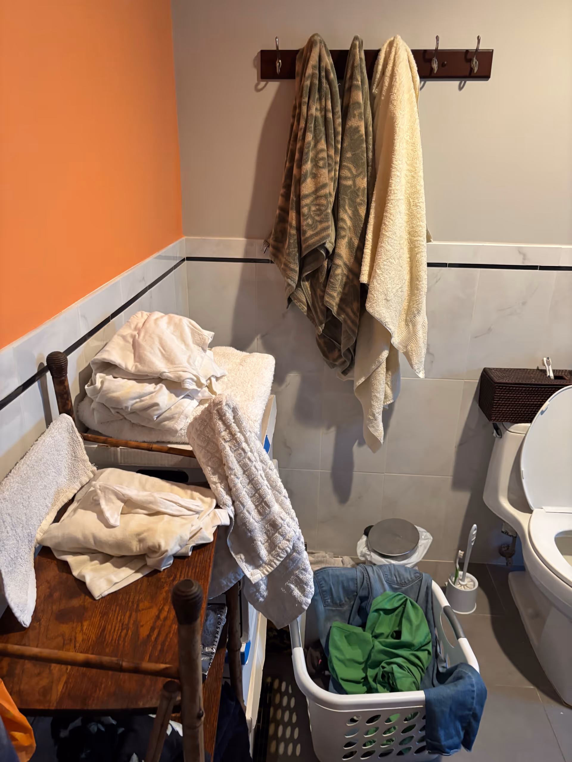 Small bathroom with towels, coats on hangers, laundry basket, and toilet.
