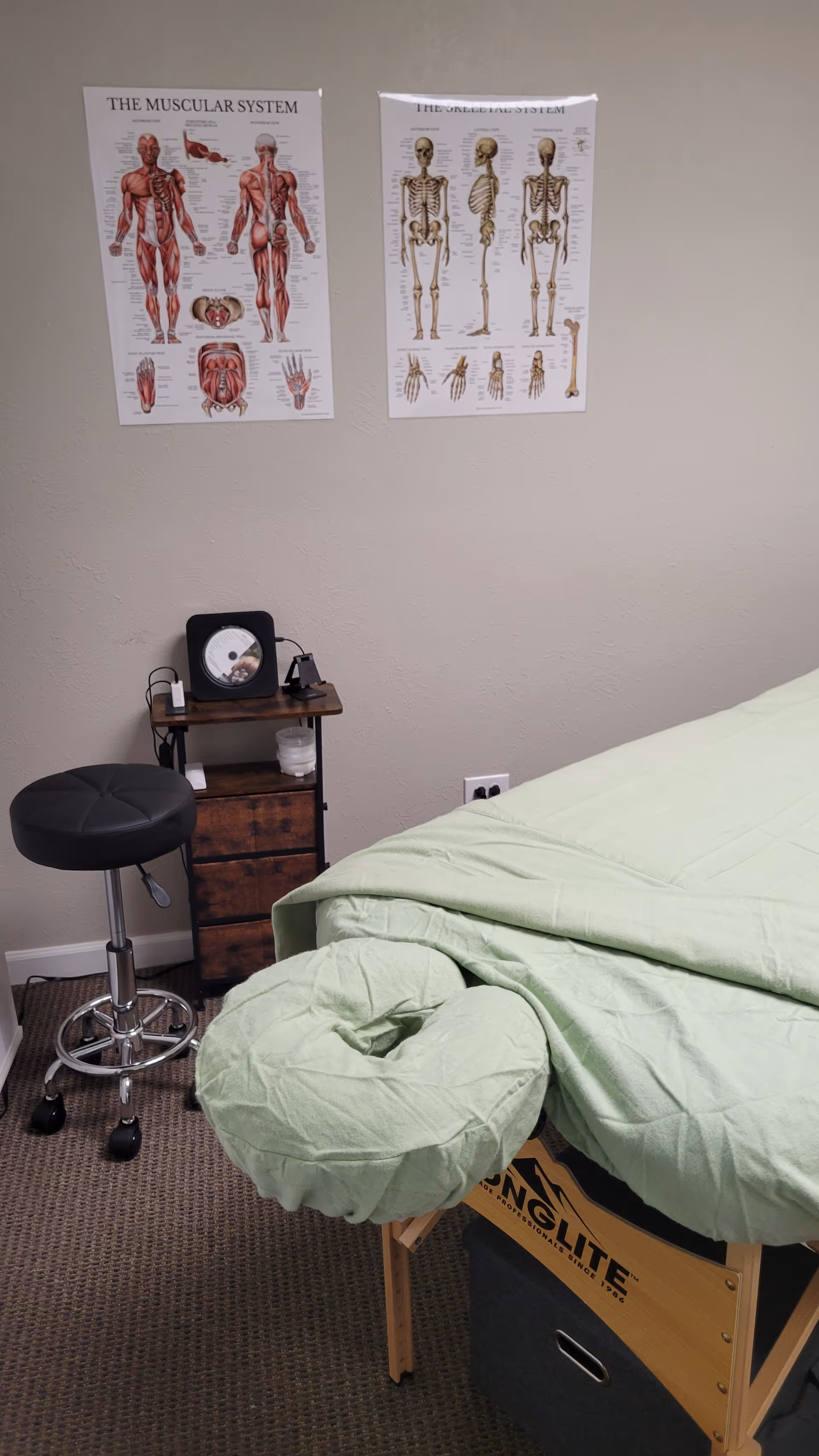 Castle Rock Massage treatment room with a massage table, wall posters, stool, and a cabinet.
