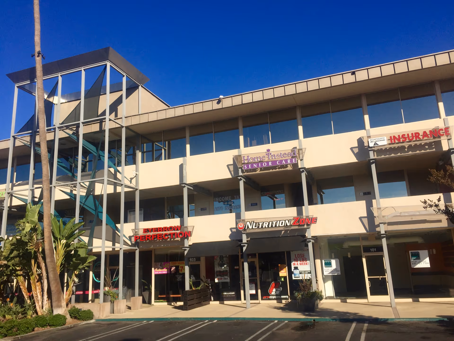 Two-story commercial building with signs including Home Instead Senior Care under a blue sky.