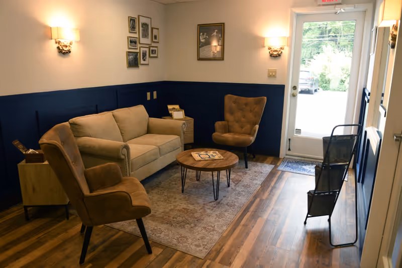 Cozy senior living lounge with sofa, two chairs, coffee table, and wall art.