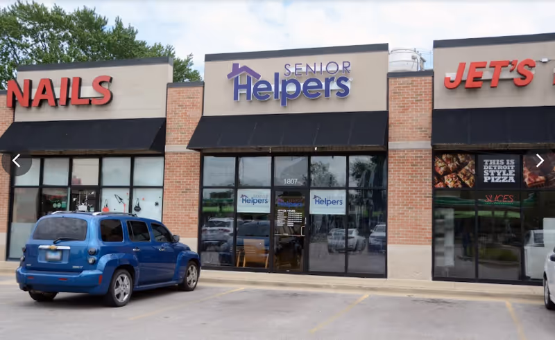 Exterior view of a strip mall with Senior Helpers storefront between Nails and Jet's.