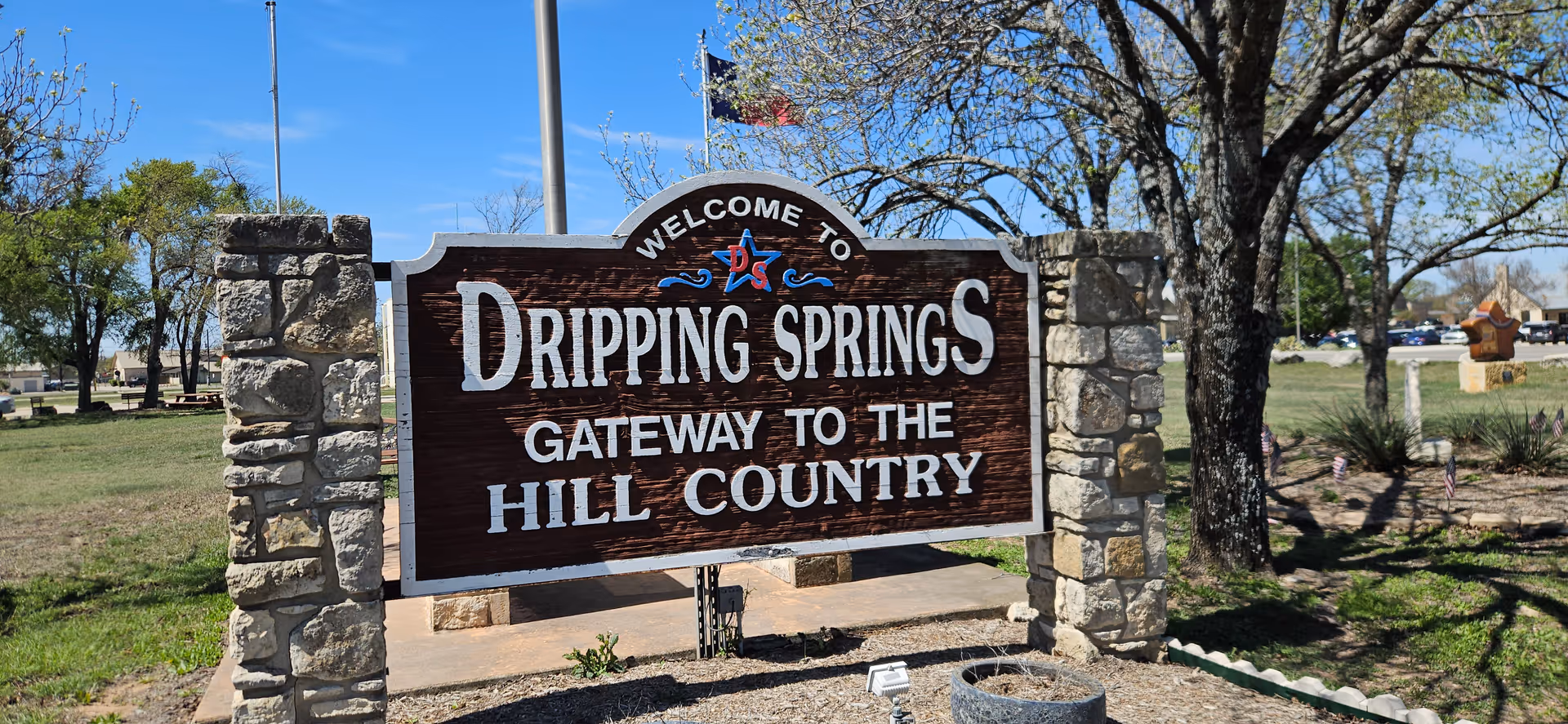 Outdoor welcome sign on stone pillars reading 'Welcome to Dripping Springs: Gateway to the Hill Country'.