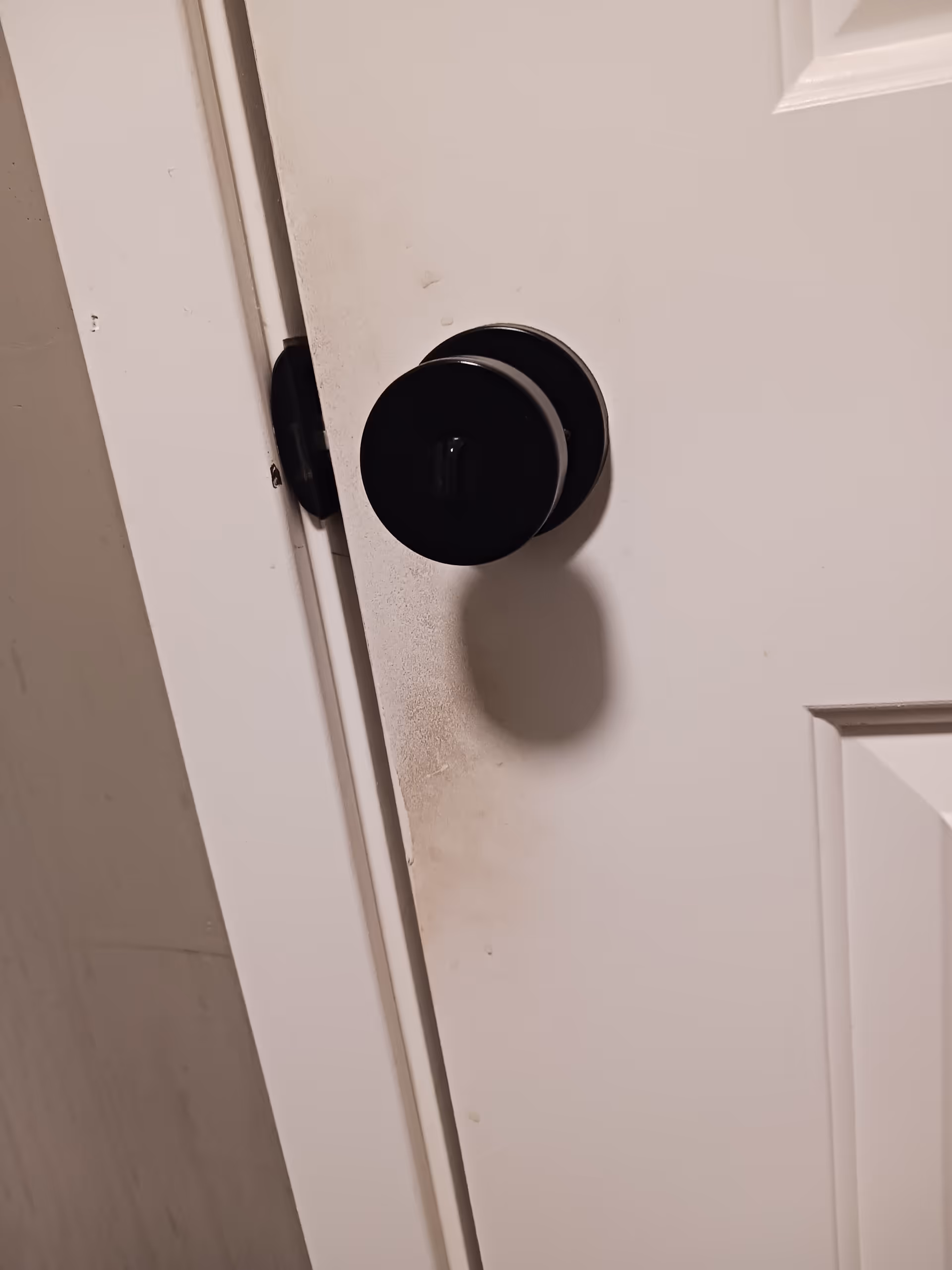 Close-up of a black door knob on a white interior door with dirt marks.