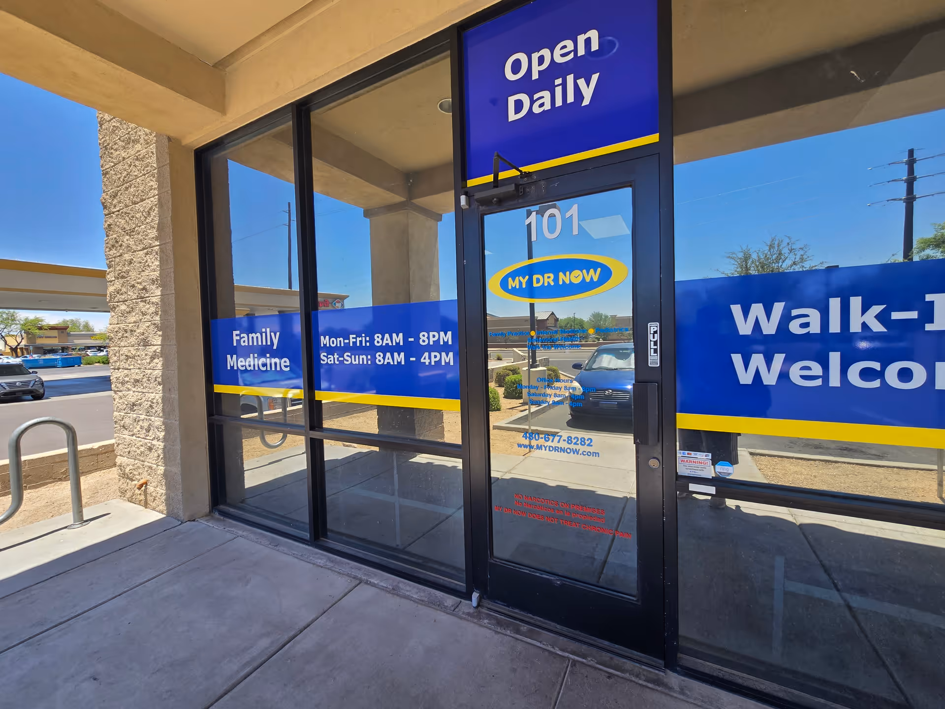 Glass storefront of a medical facility with Open Daily and Walk-Ins Welcome signs.