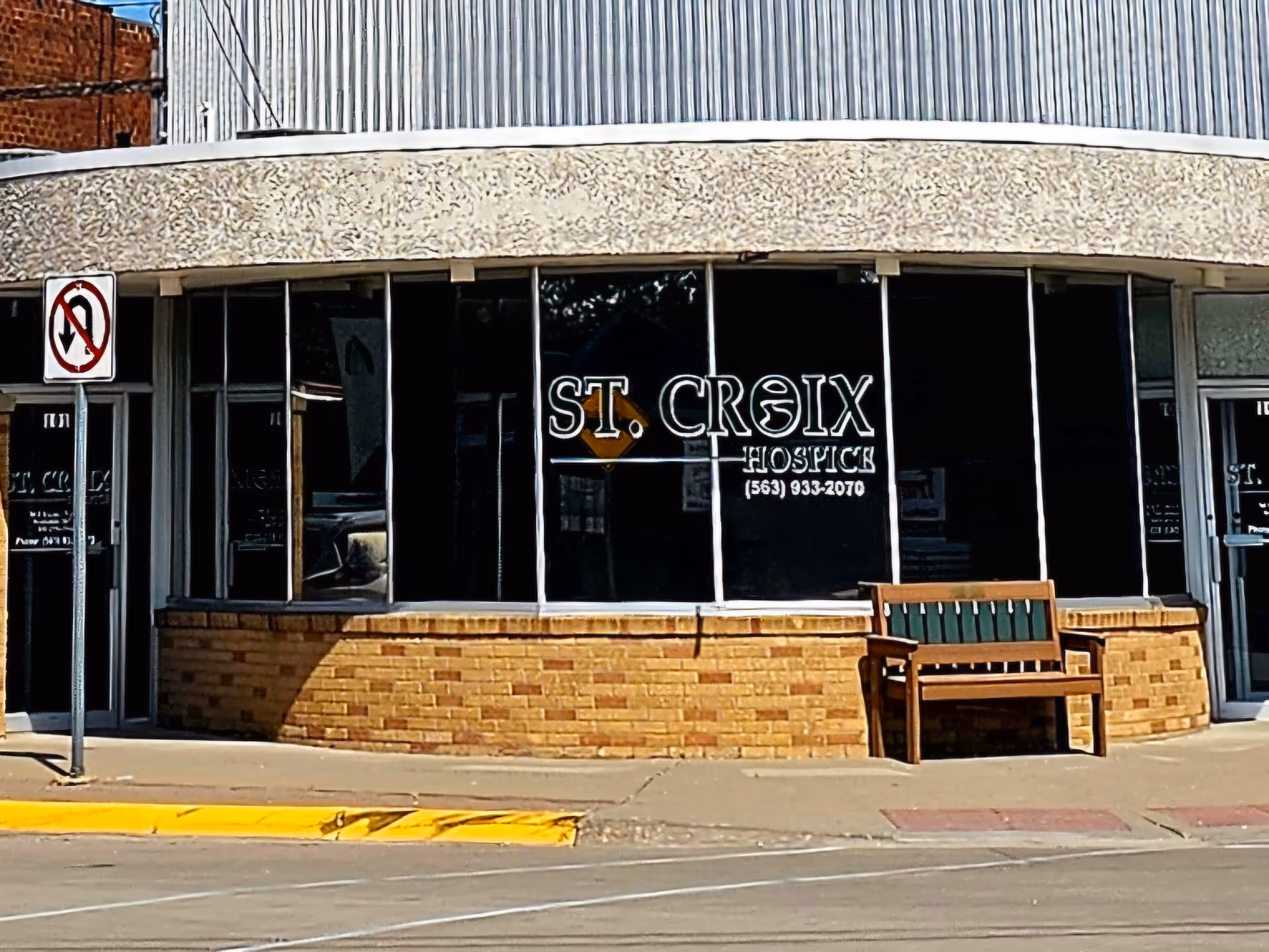 Exterior storefront of St. Croix Hospice with brick base, large windows, and a bench outside.