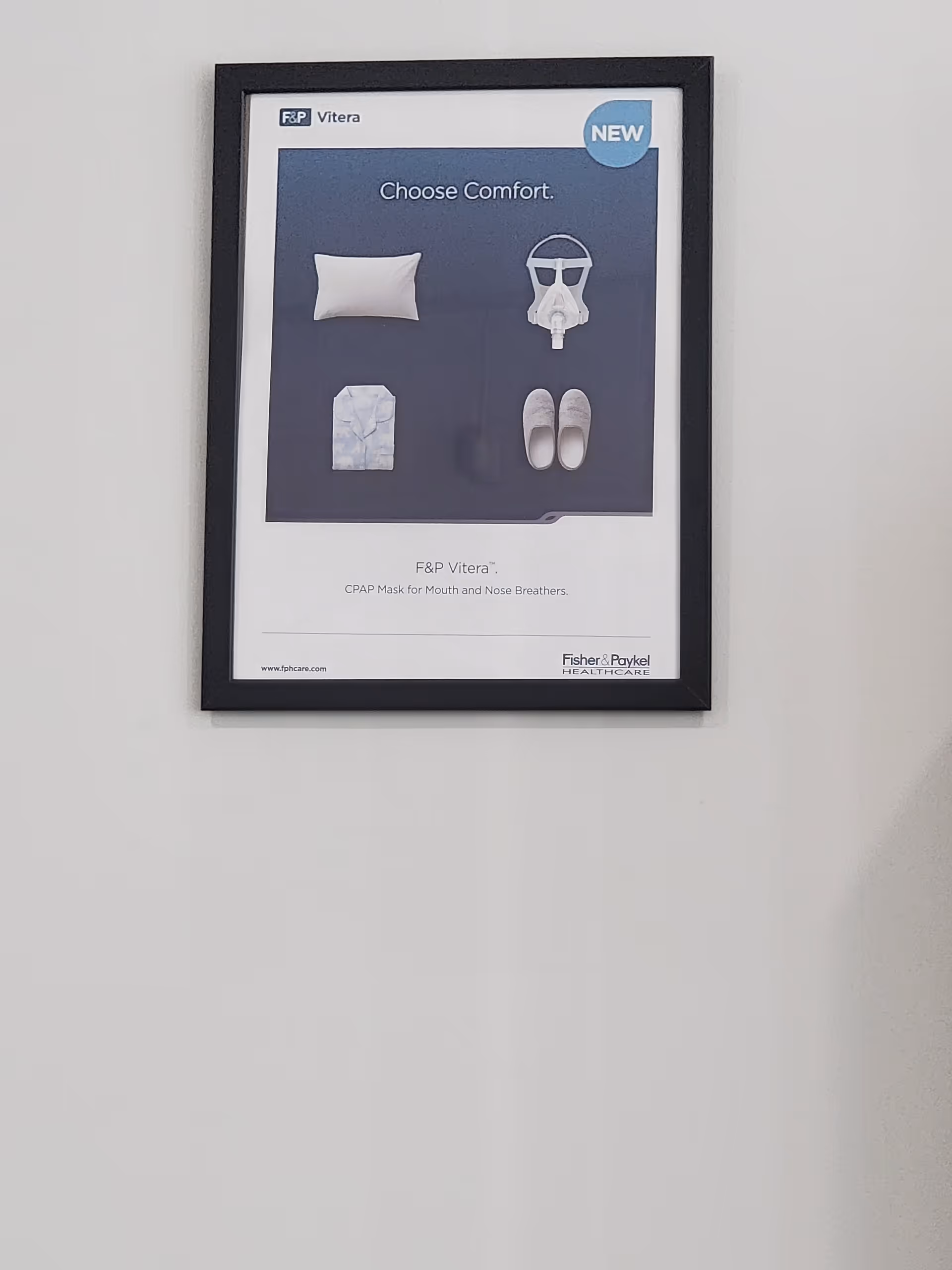 Framed poster on a white wall illustrating CPAP gear with pillow, mask, and slippers.