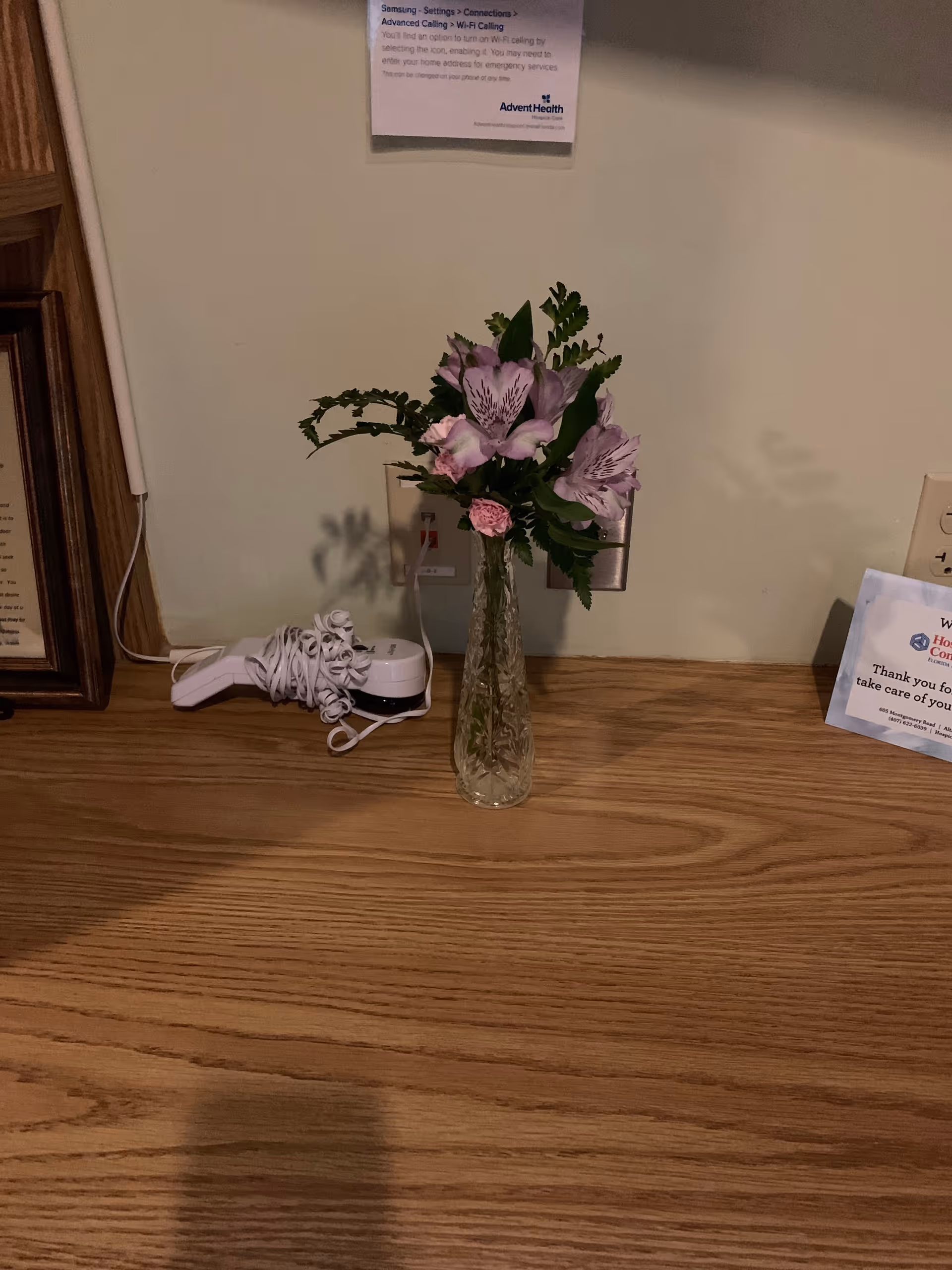 Wooden counter with a glass vase of pink flowers and a white phone.