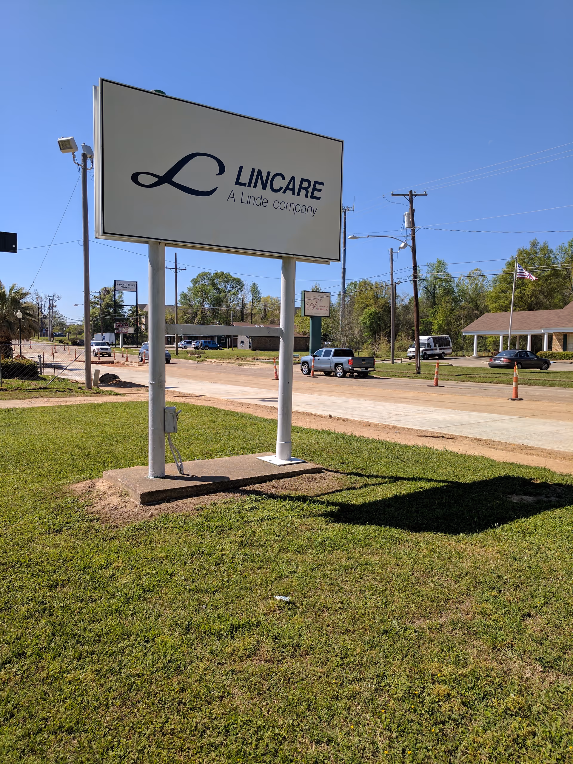 A large LINCARE sign stands on a grassy lot near a road with a building behind