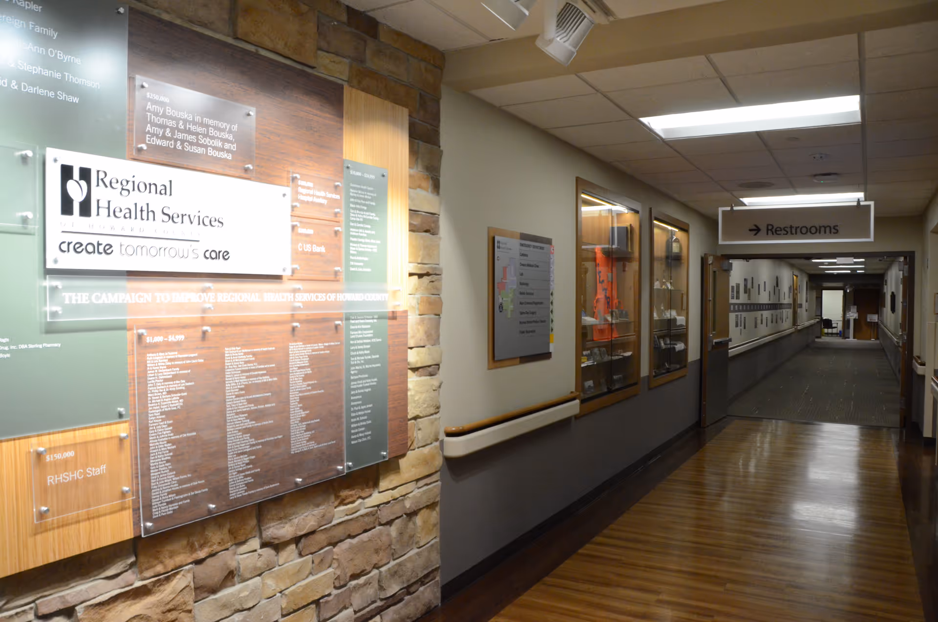 Indoor corridor of Regional Health Services with stone wall, display boards, and a Restrooms sign.