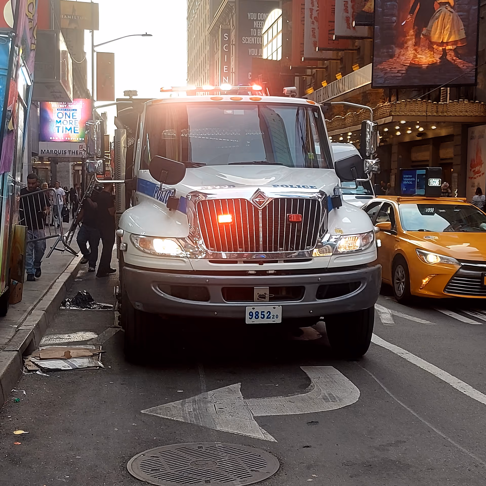 A large white emergency vehicle with lights dominates a busy city street beside a yellow taxi.