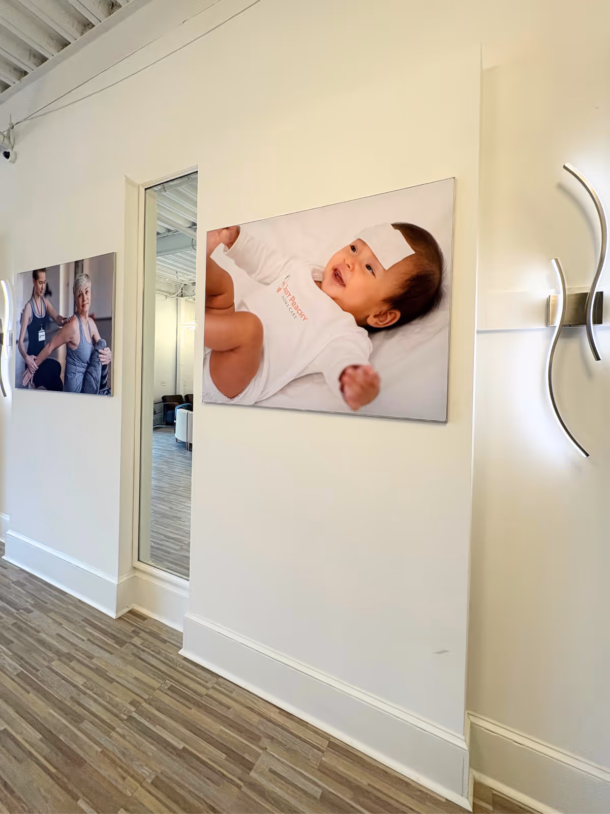 White-walled hallway with wood-like flooring and large wall photos in a senior care facility.