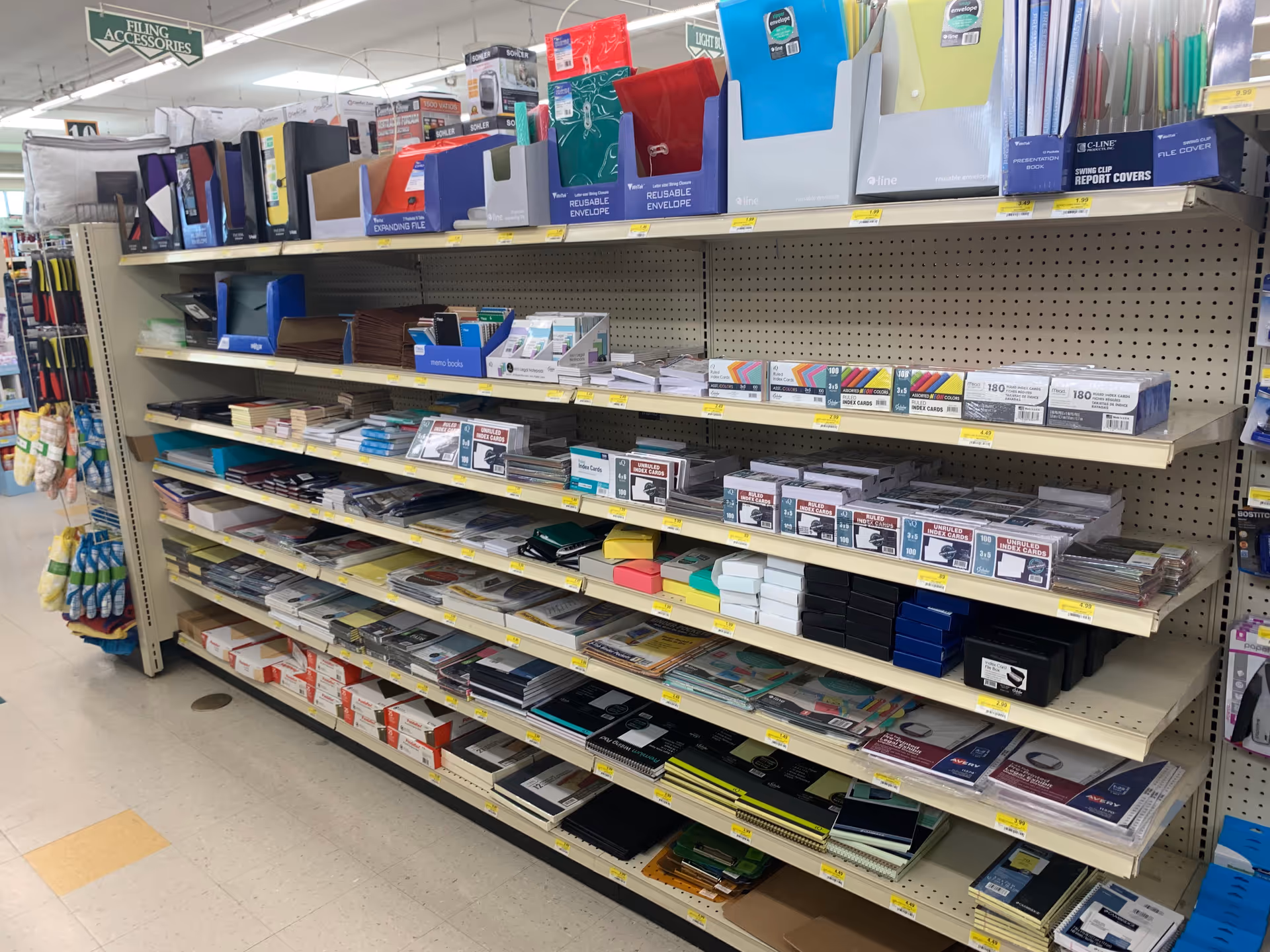 Aisle of office supplies with folders, notebooks, and envelopes on metal shelves in Discount Drug Mart.
