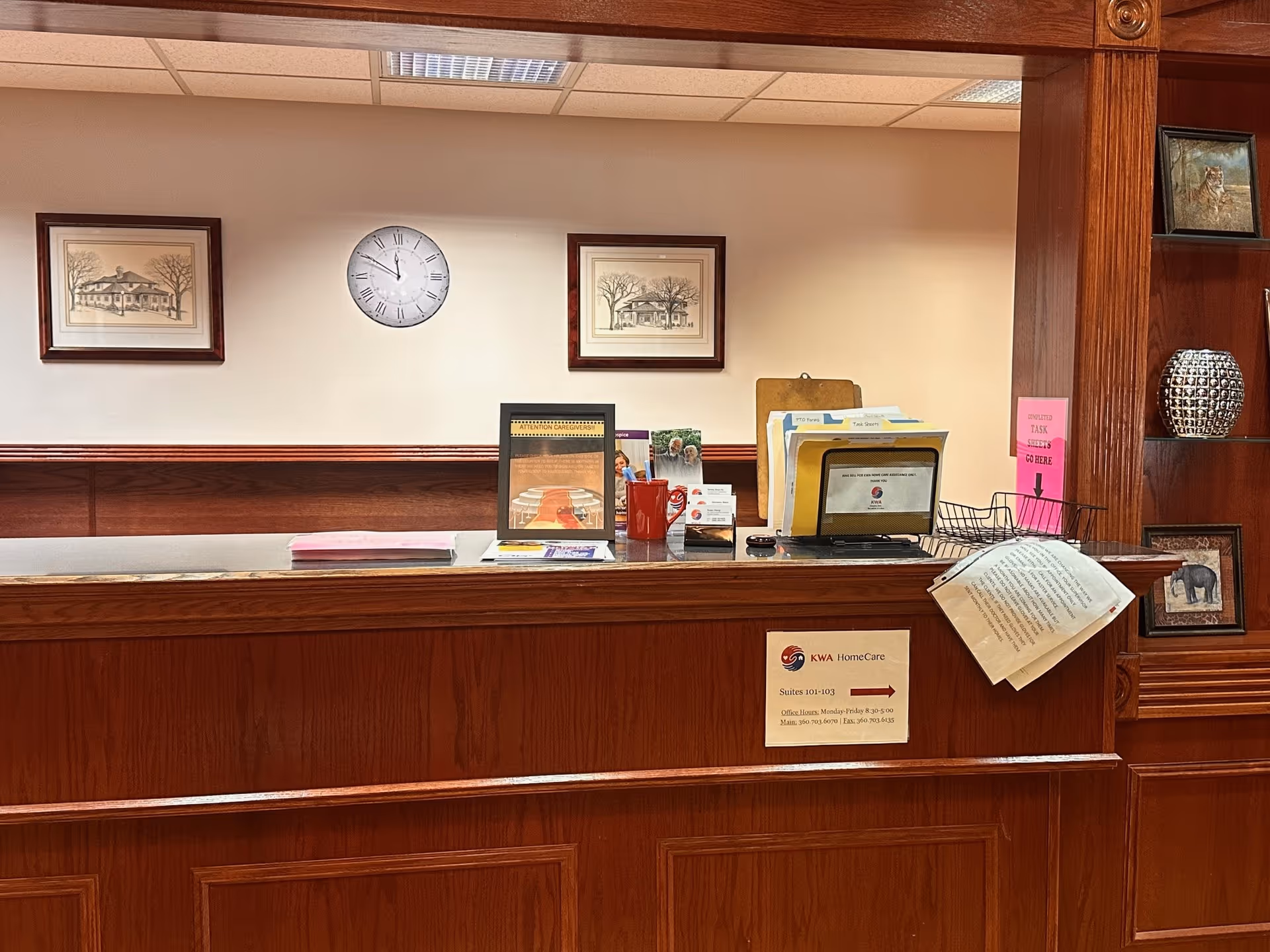 Wood-paneled reception desk in a lobby with clock, framed art, and files.