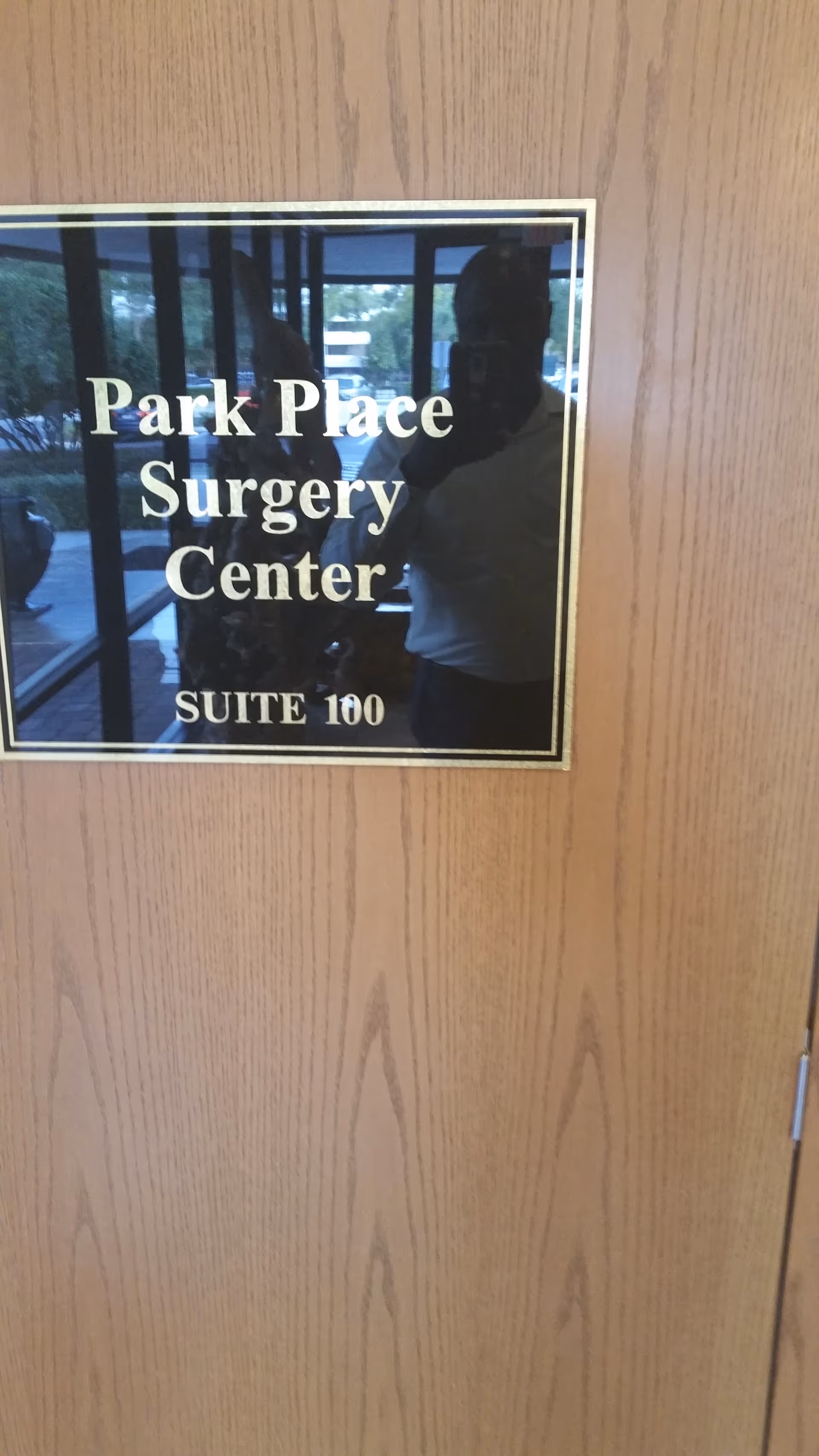 Wooden door plaque reads Park Place Surgery Center Suite 100; reflection visible.